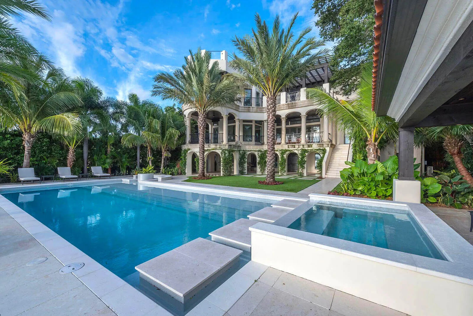 Luxury residential pool and spa with neoclassical mansion, palm trees, and manicured lawn in St Petersburg, Florida.