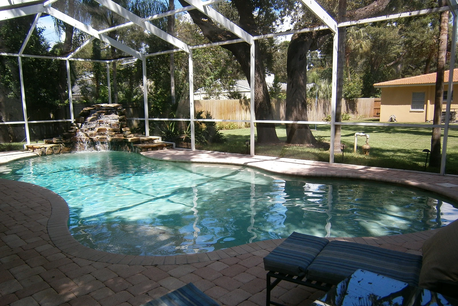 Luxury screened pool with cascading waterfall, brick deck, and mature trees in Saint Petersburg residential setting