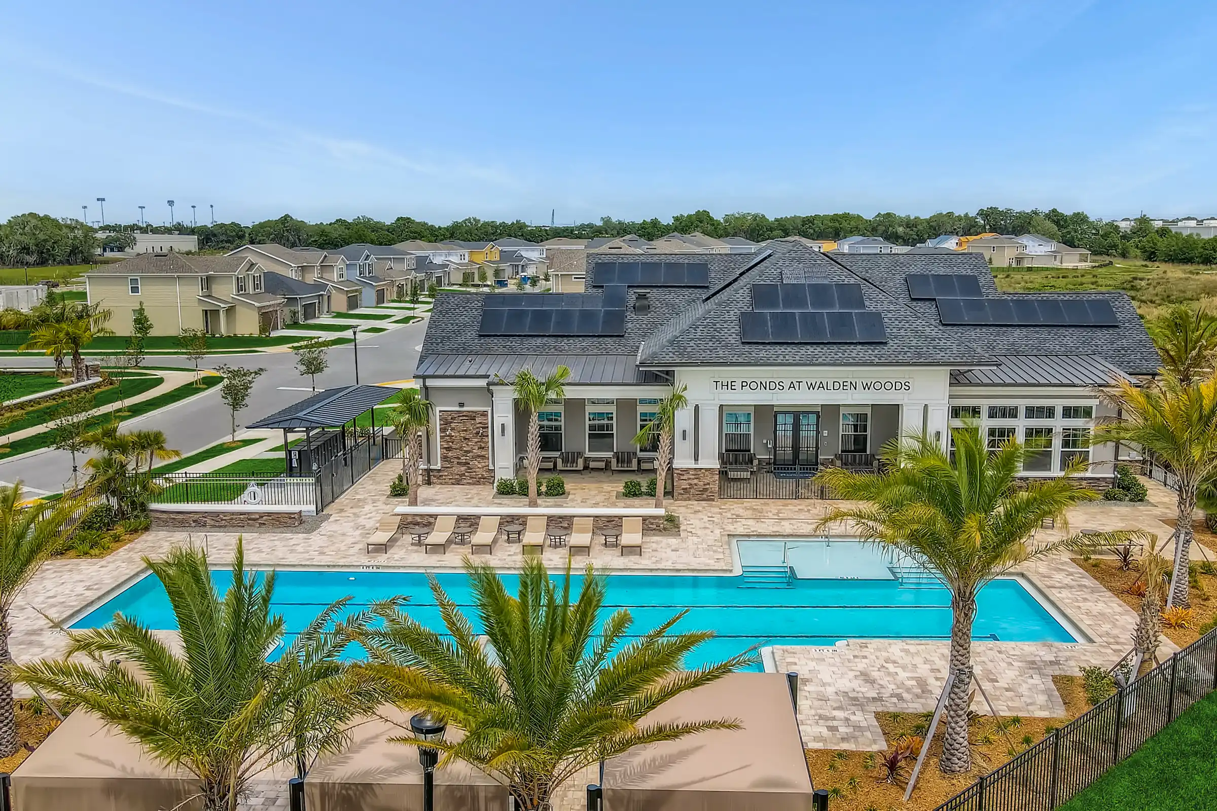 Modern clubhouse with solar panels overlooking illuminated resort pool, lounge seating, and palm-lined deck in St Petersburg residential community.