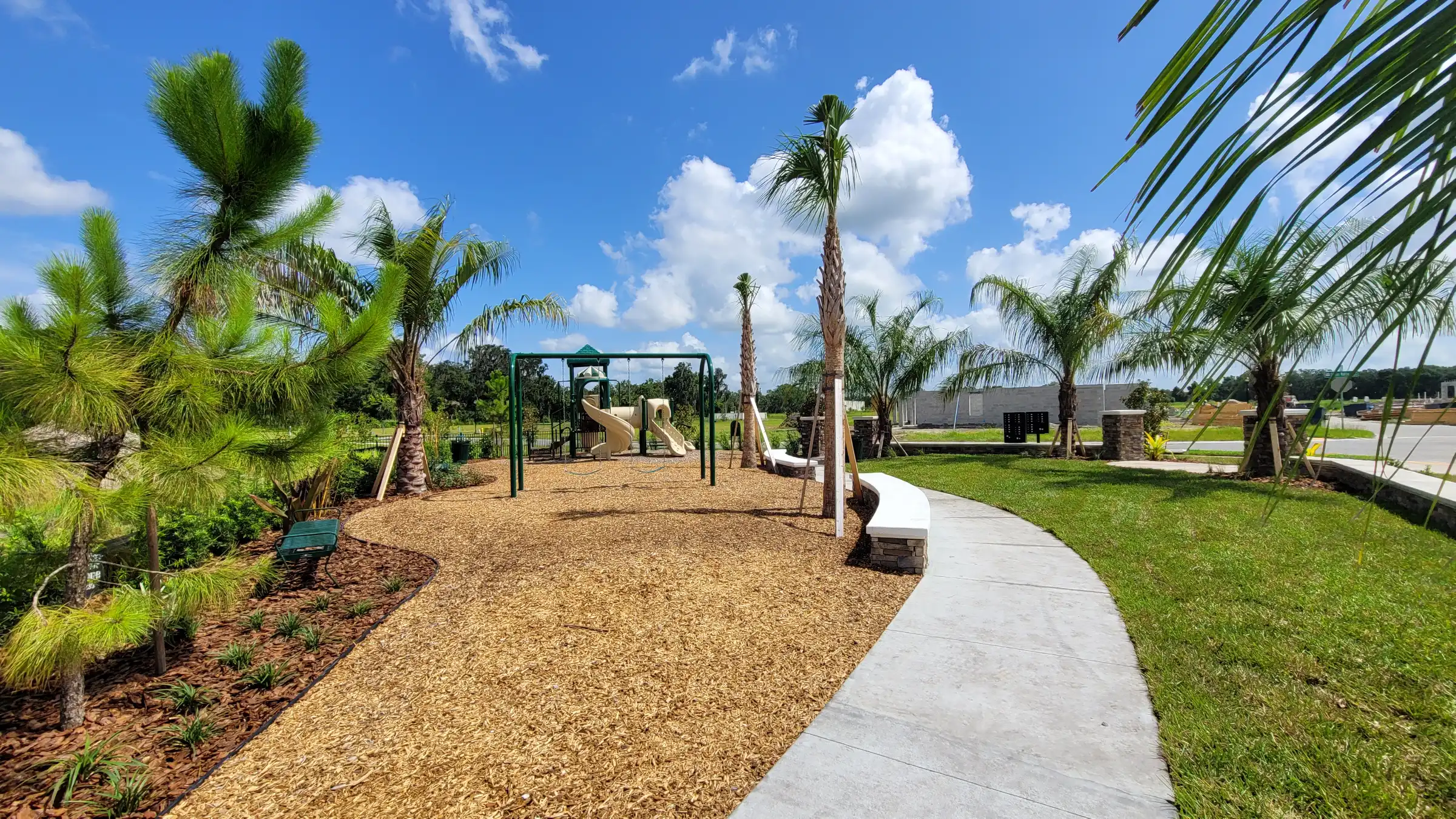 Modern playground with palm trees, sand surface, and curved concrete pathway in luxury St Petersburg residential community with manicured landscape design.
