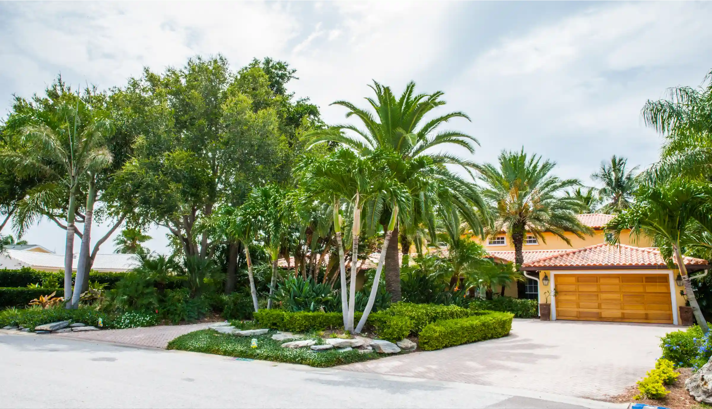 Luxury residential home with golden stucco exterior, wooden garage doors, and mature palm trees lining brick driveway in St Petersburg, FL.