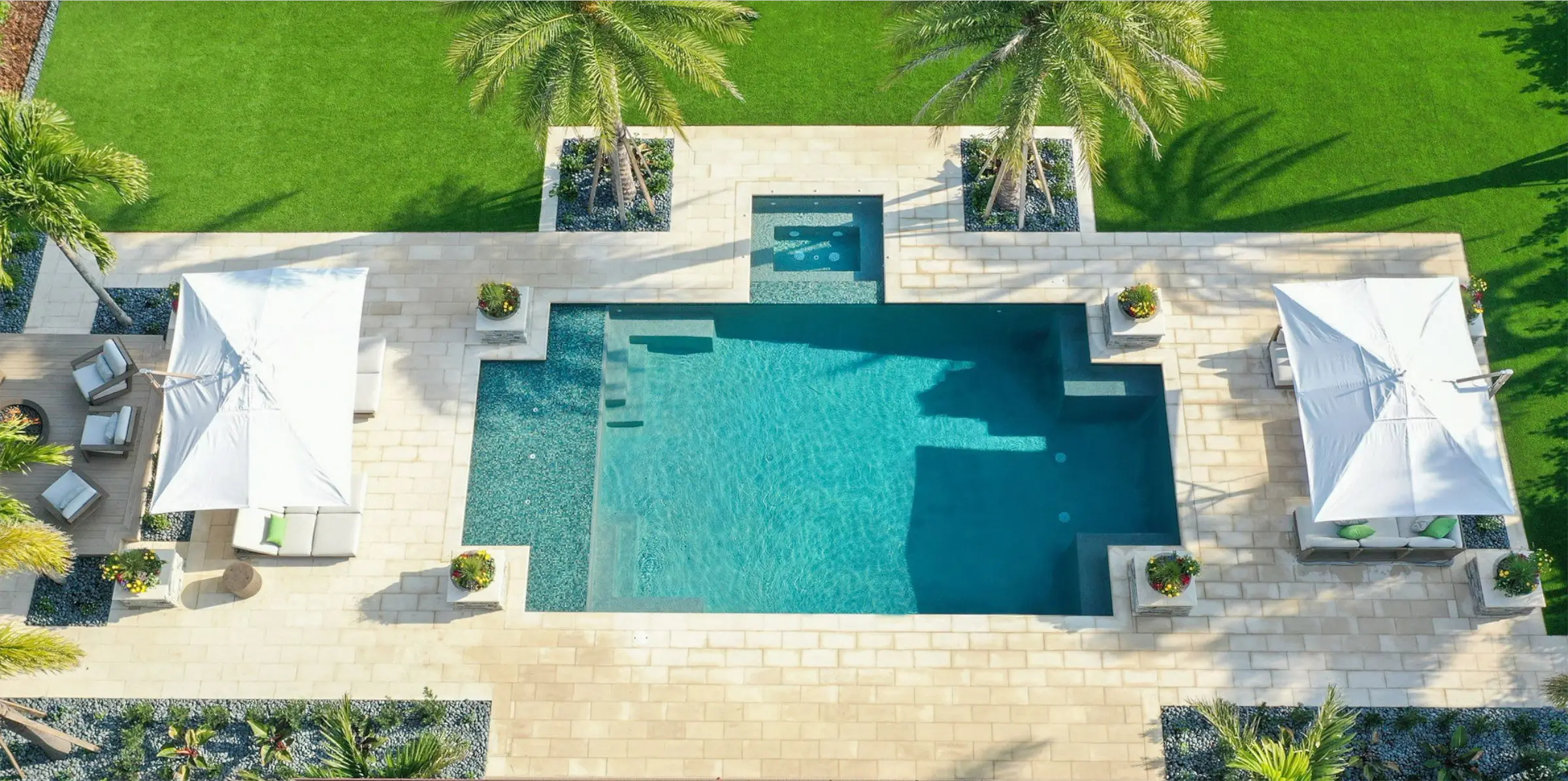 Aerial view of luxury pool design featuring geometric spa sections, limestone decking, white shade structures, and manicured lawn in St Petersburg residential community