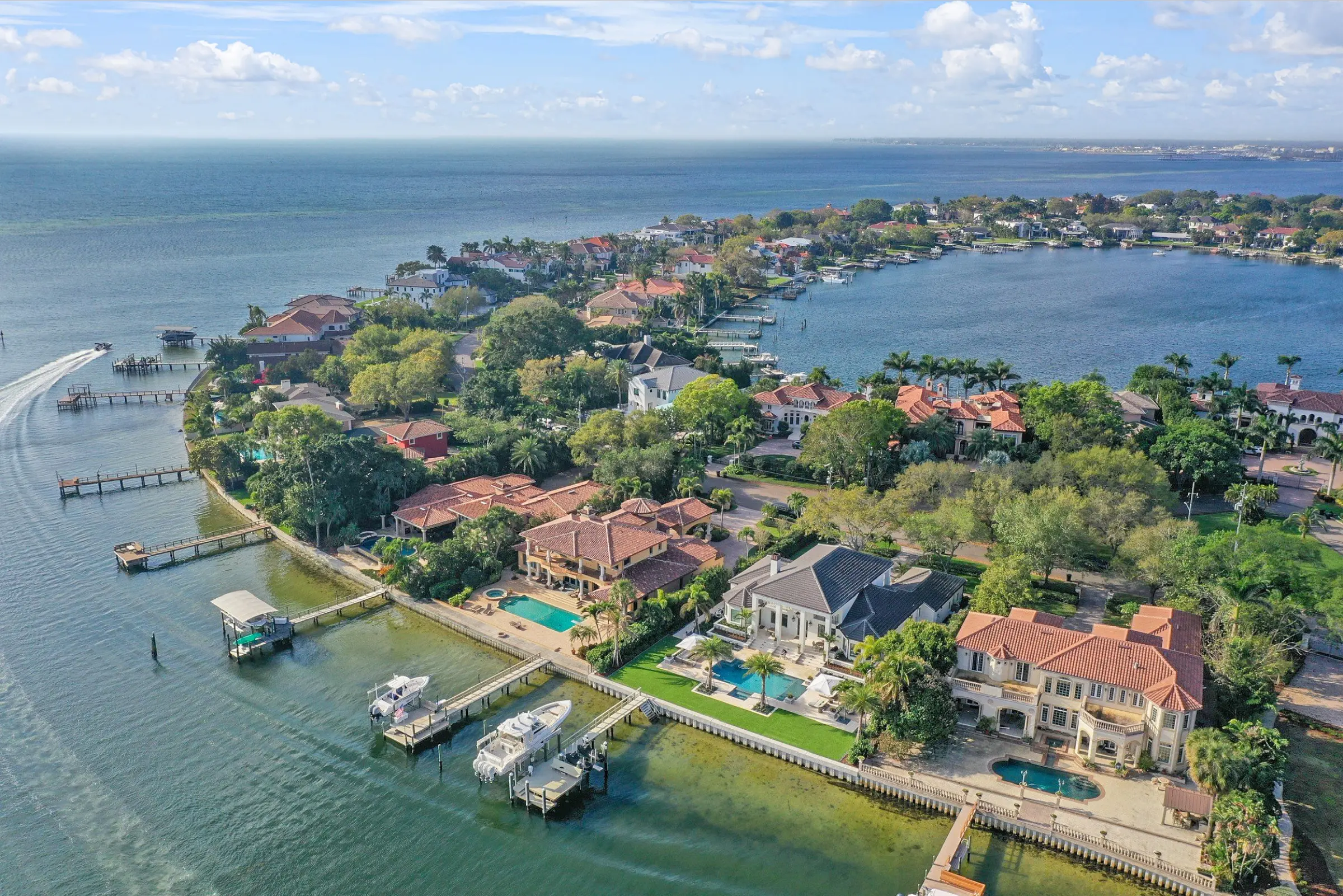 Aerial view of luxury waterfront homes with orange tile roofs along Tampa Bay, featuring pool design and manicured landscapes in St Petersburg.