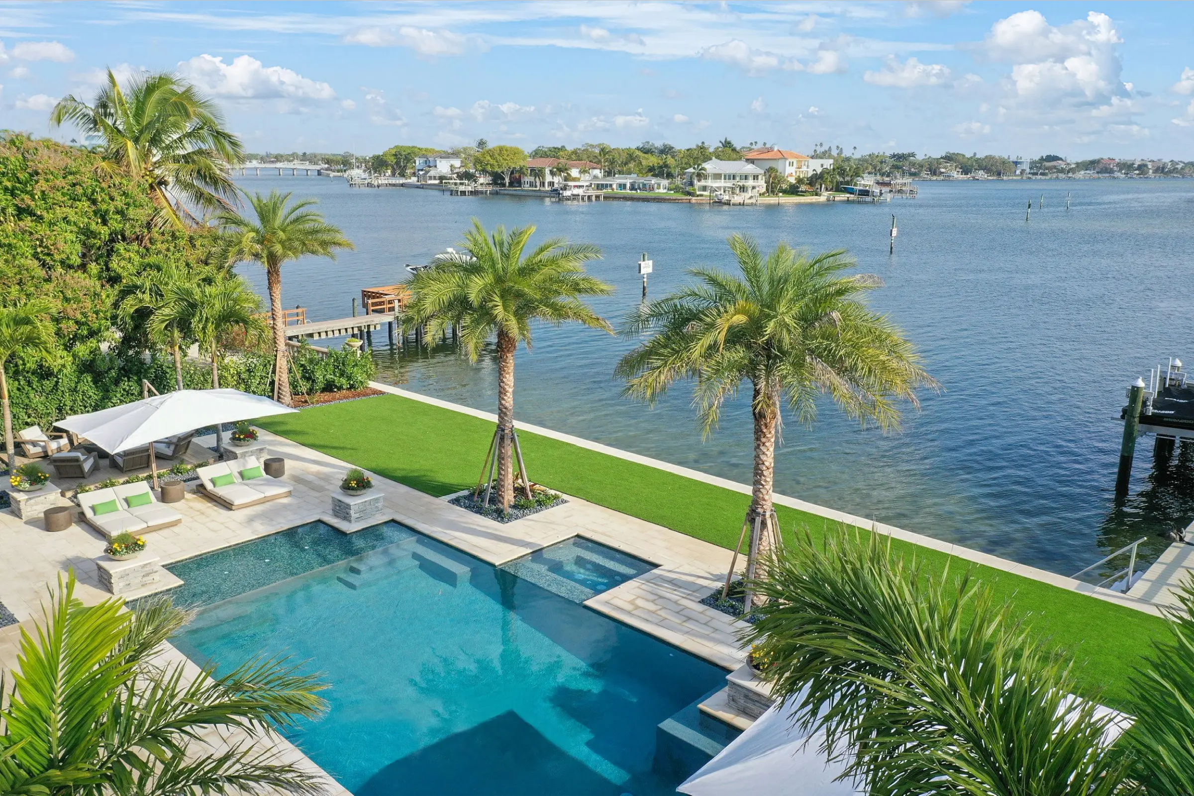 Luxury waterfront pool and spa with manicured lawn, palm trees, and St Petersburg bay views with residential community across the water.