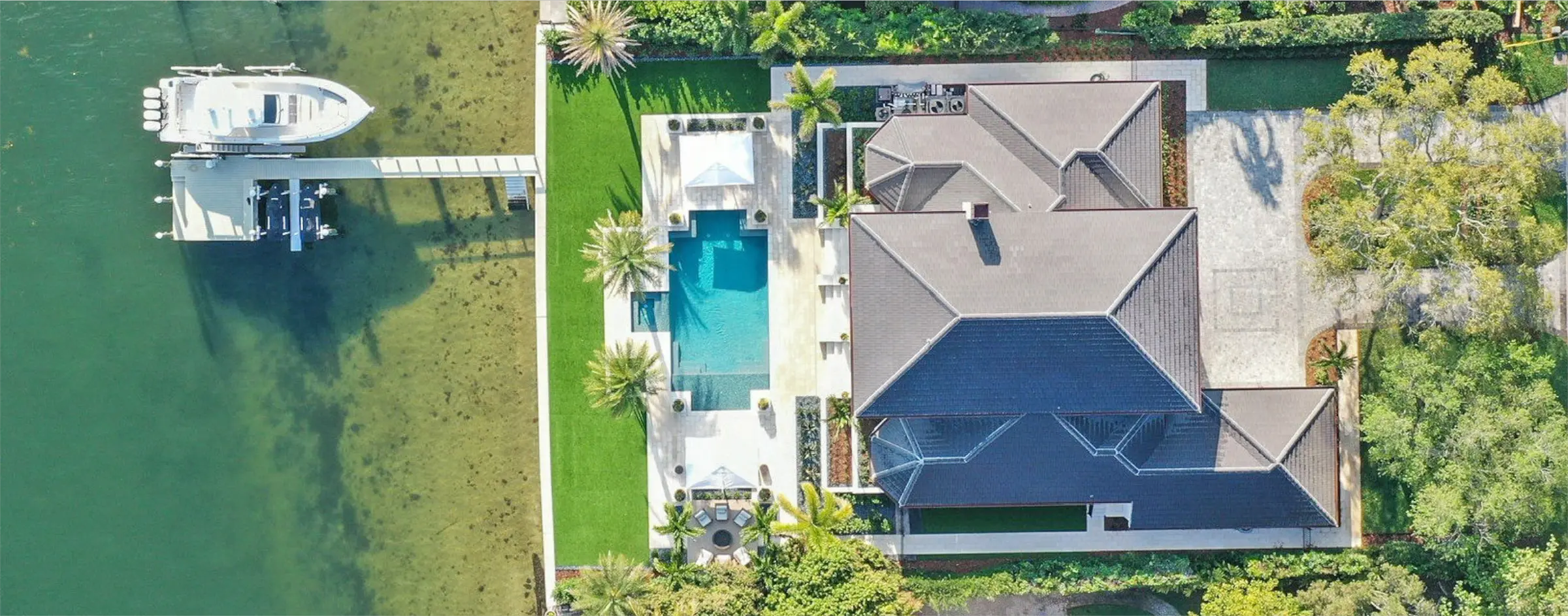 Aerial view of luxury waterfront home with navy roof, sparkling pool, manicured lawn, and private boat dock in St Petersburg, FL.