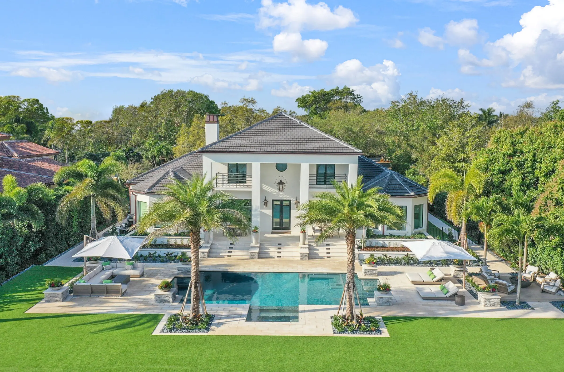Luxury white colonial home with turquoise pool, palm trees, and manicured lawn in St Petersburg, Florida residential community.