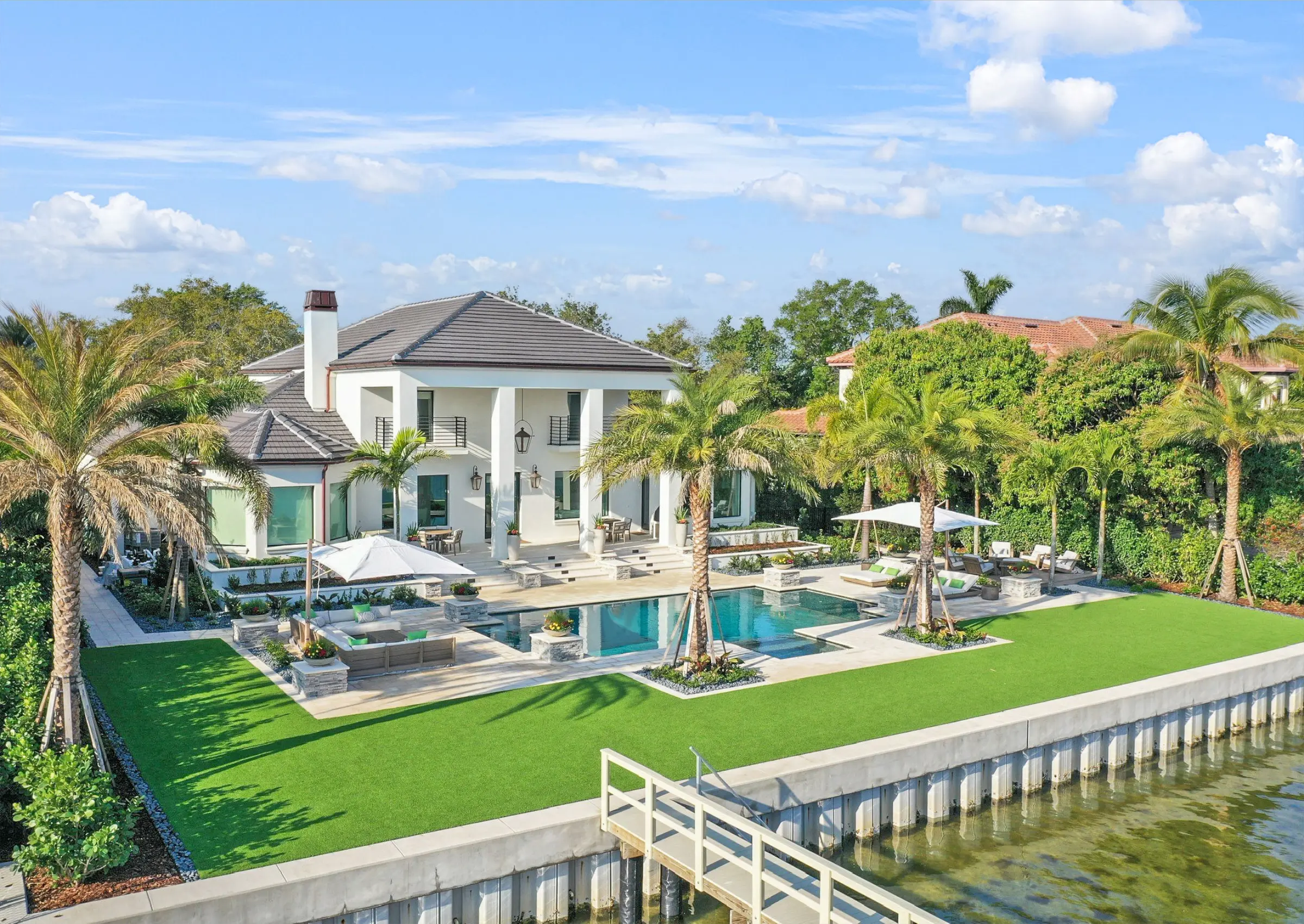 Luxury waterfront home with turquoise pool, manicured lawn, palm trees, and modern architecture overlooking canal in St Petersburg, FL.