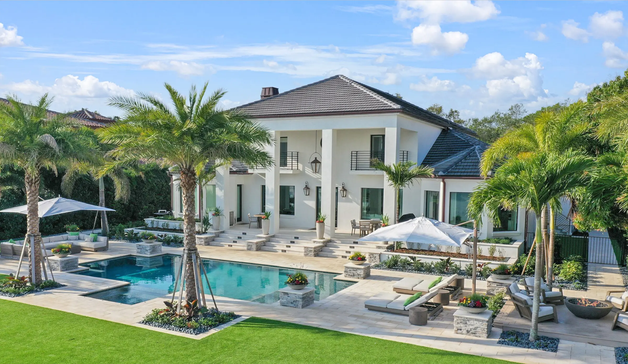 Contemporary white house with dark roof overlooking turquoise pool and spa, surrounded by palm trees and manicured lawn in St Petersburg luxury residential community