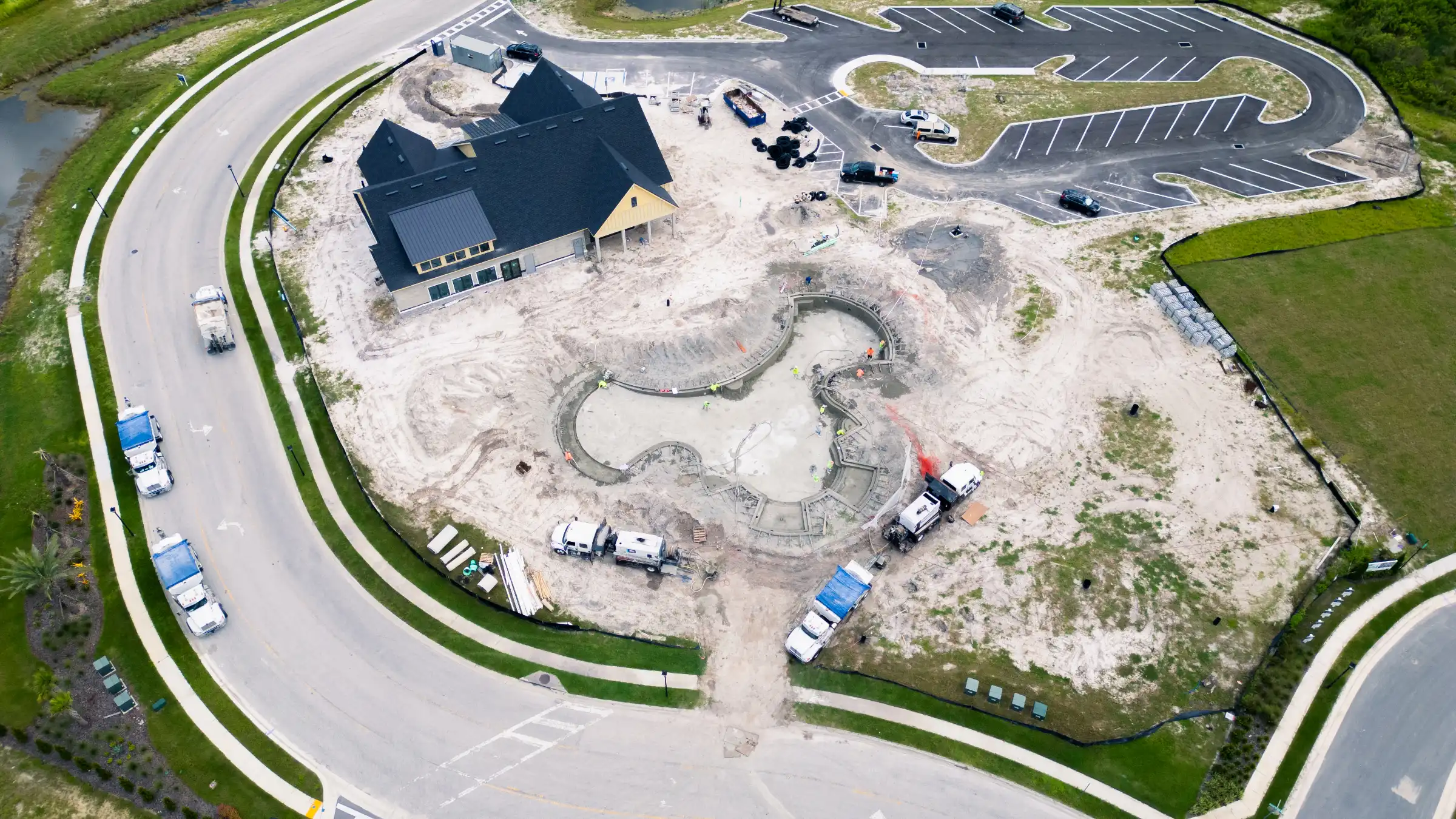 Aerial view of luxury pool design under construction with curved concrete features, residential home with dark roof, and finished parking areas in St Petersburg, FL.