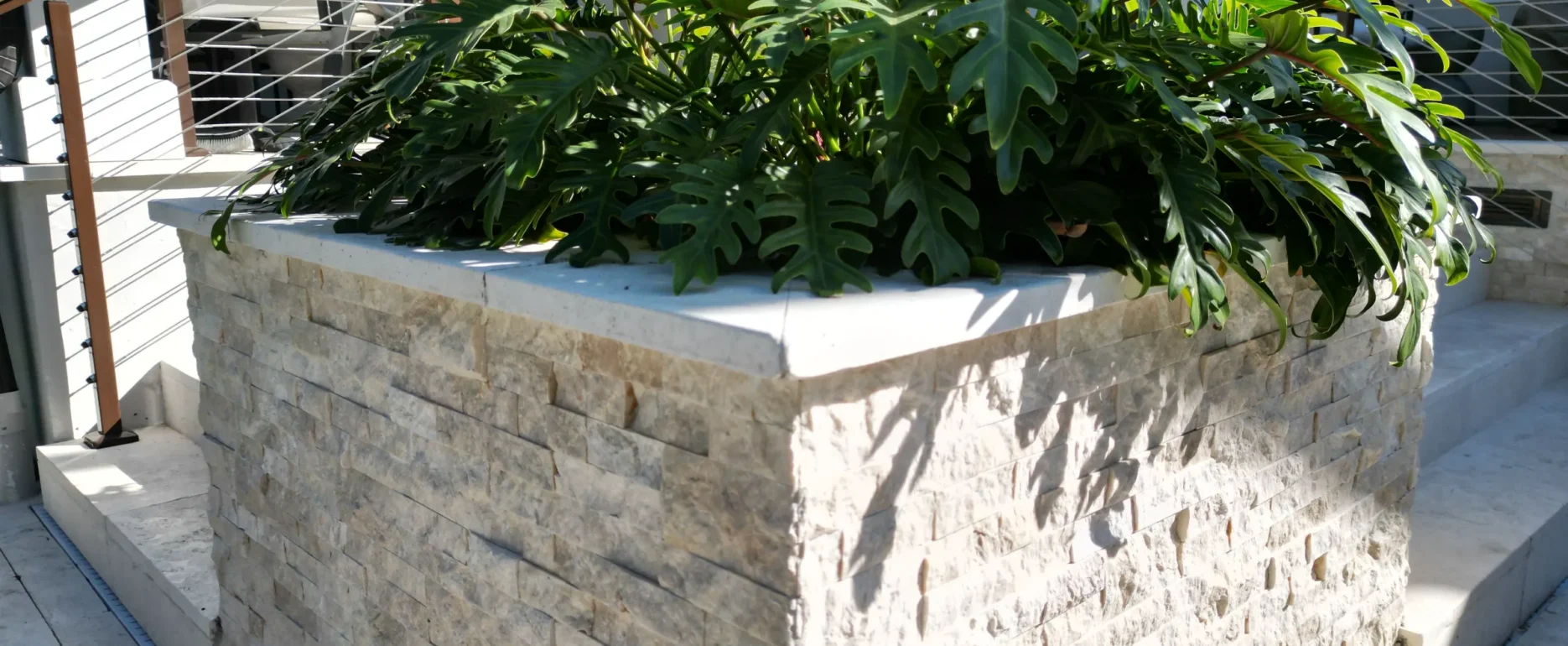 Curved stone planter with lush tropical plants on a coastal residential terrace in St Petersburg, FL, featuring luxury landscape design.