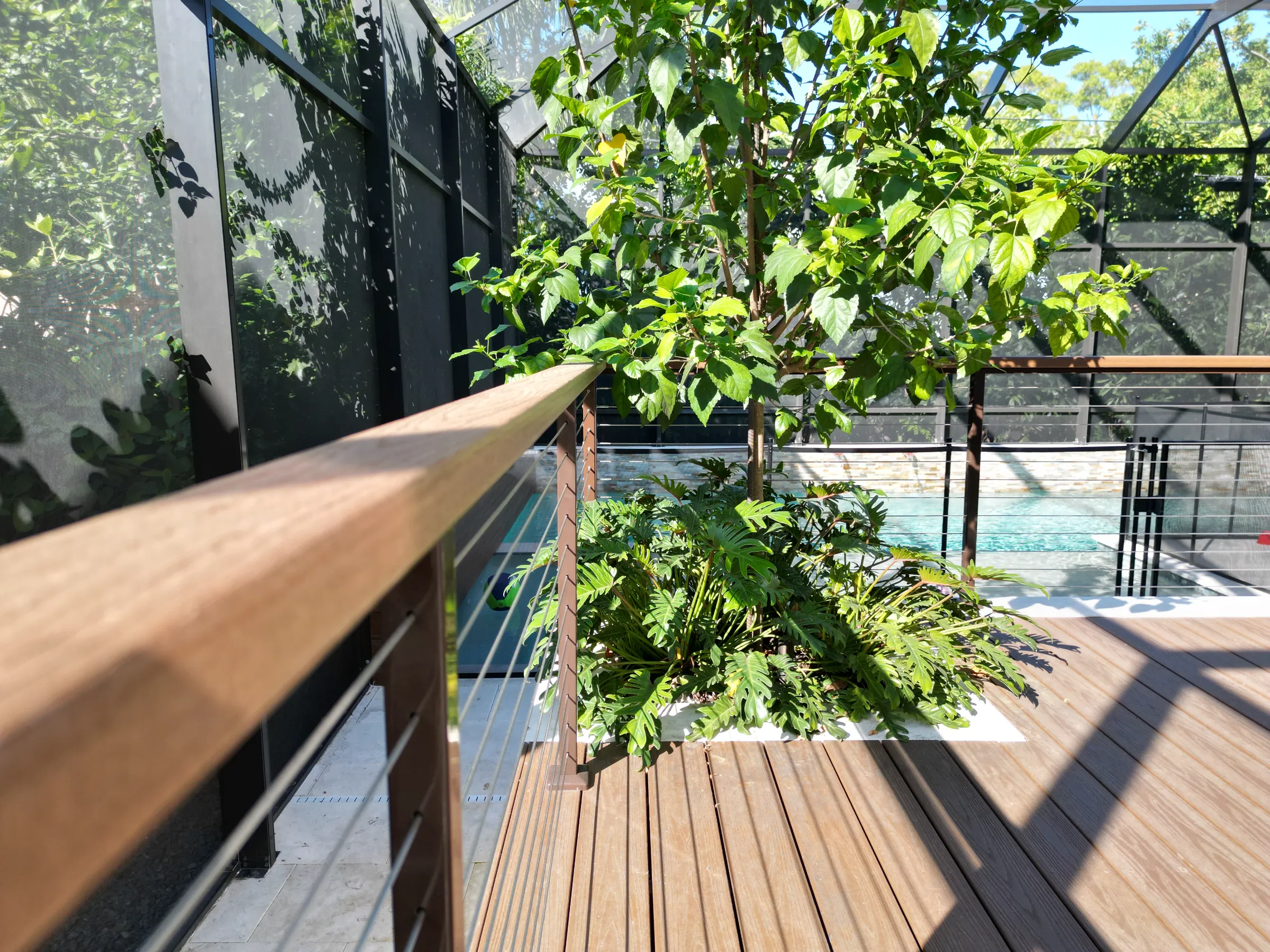 Luxury pool deck with wooden railing, lush climbing vines, and water views, showcasing refined outdoor living design in St Petersburg residential community.