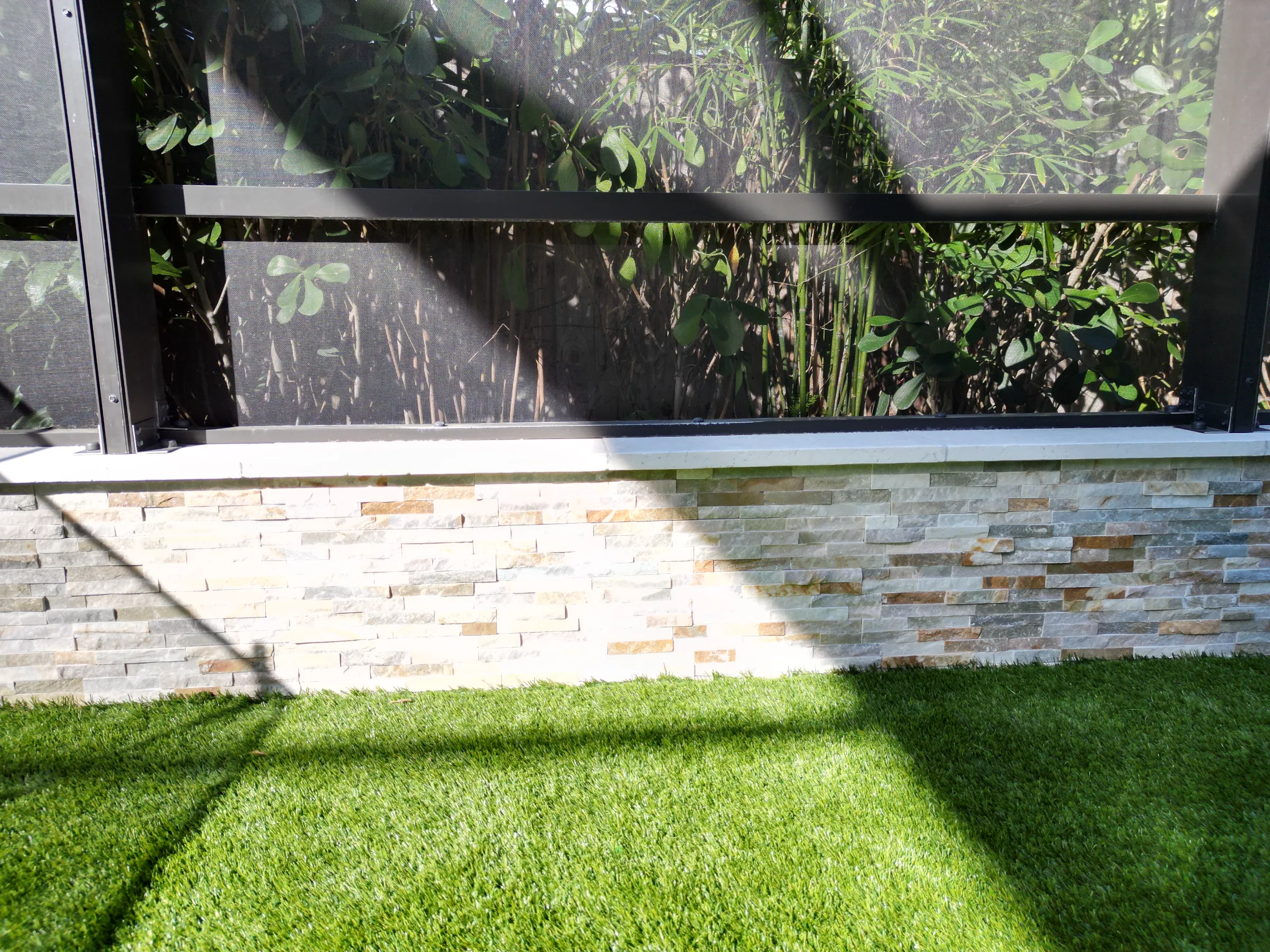 Modern luxury landscape design featuring stacked stone retaining wall with manicured lawn and contemporary black privacy screening in St Petersburg residential community.