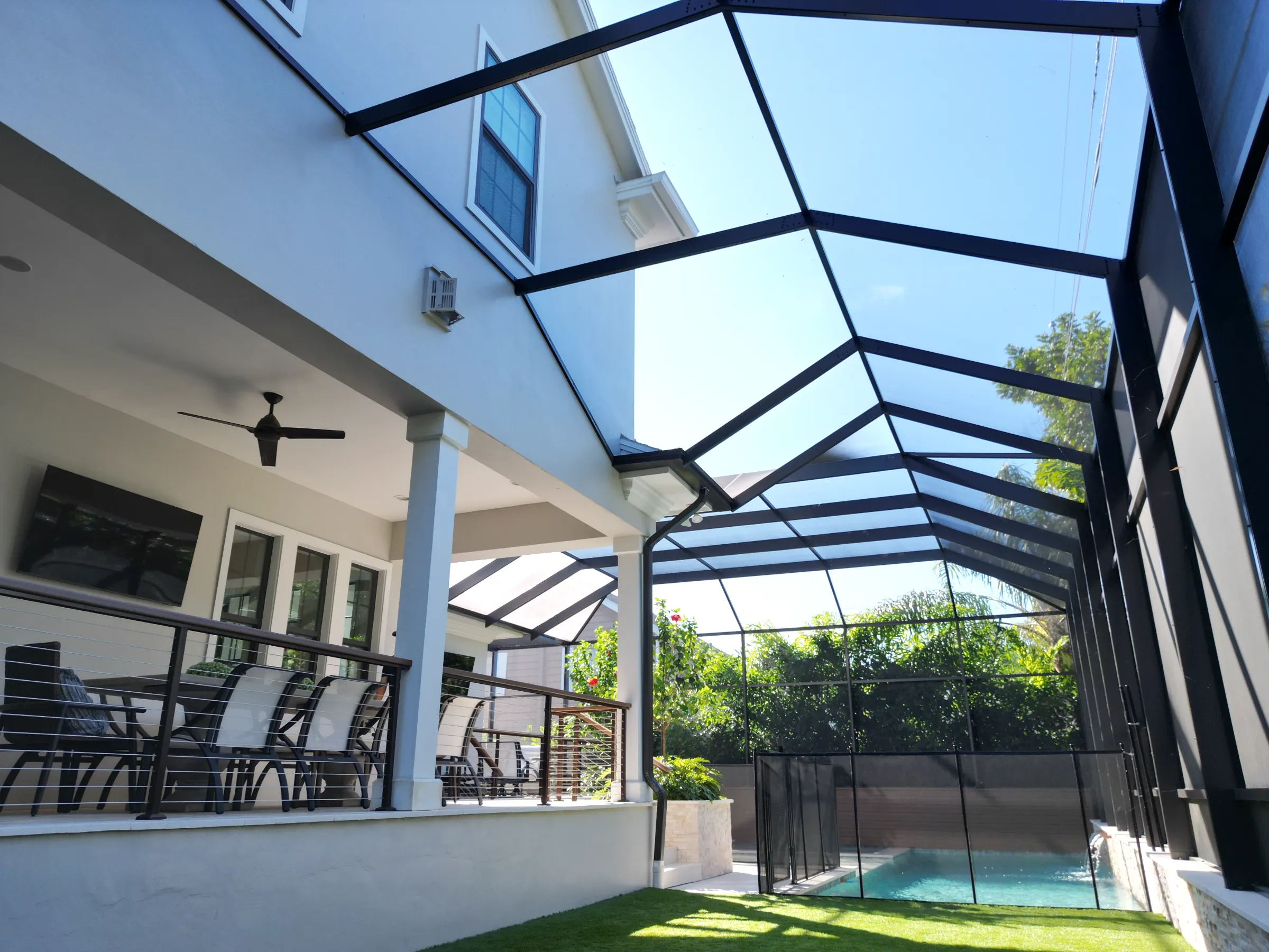 Contemporary home with black-framed glass pool enclosure overlooking manicured lawn and landscaping in St Petersburg residential community.
