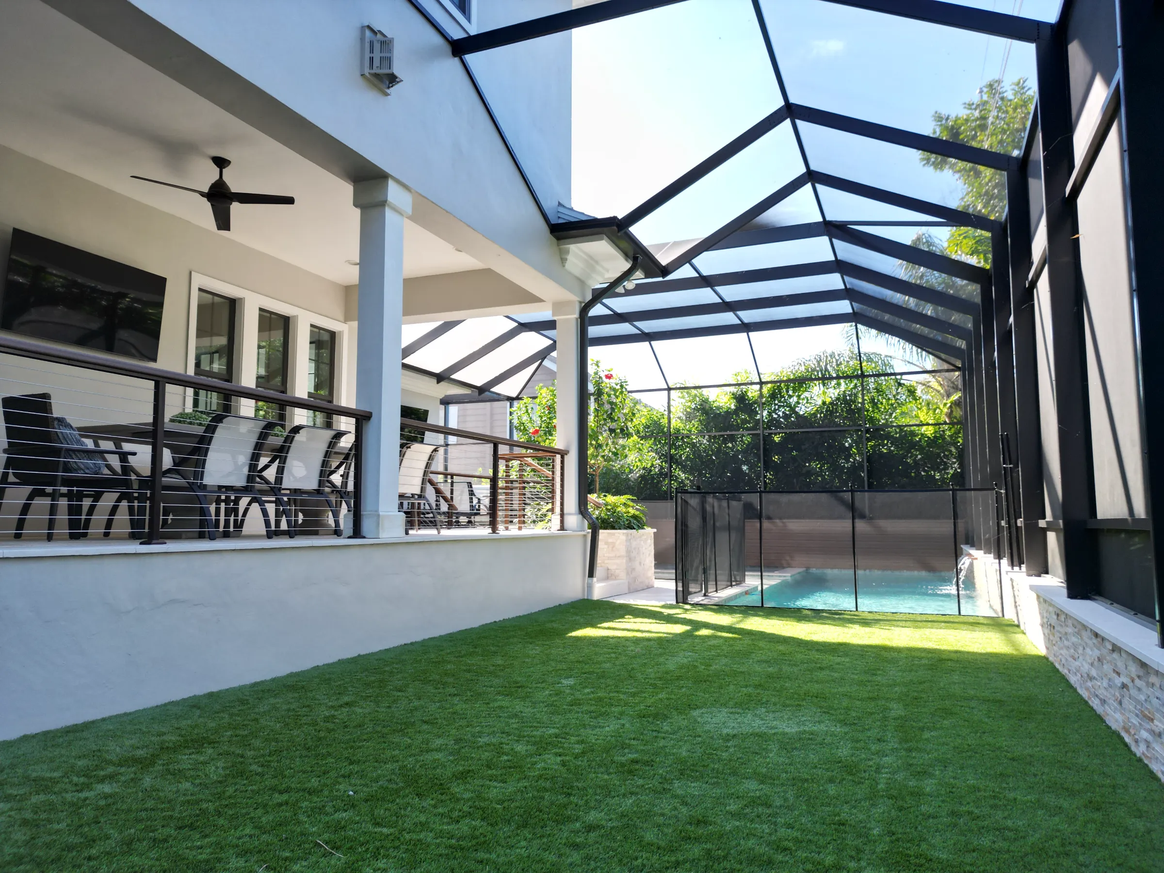 Contemporary home with glass-roofed pool enclosure, manicured lawn, and black metal railings overlooking residential pool area in St Petersburg, FL.
