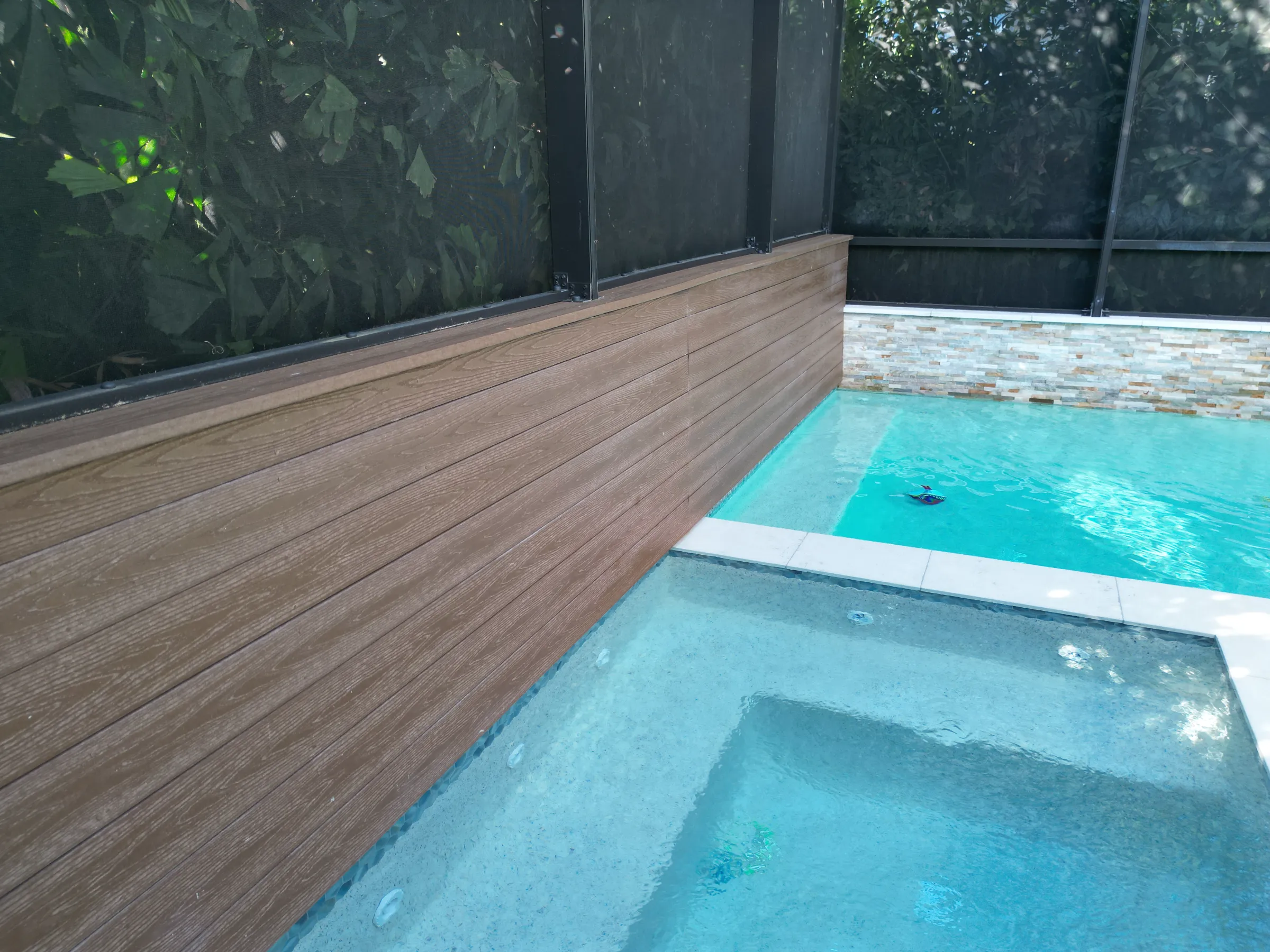 Luxury pool design featuring turquoise water, wooden deck, and stone spa in St Petersburg residential community with screened enclosure