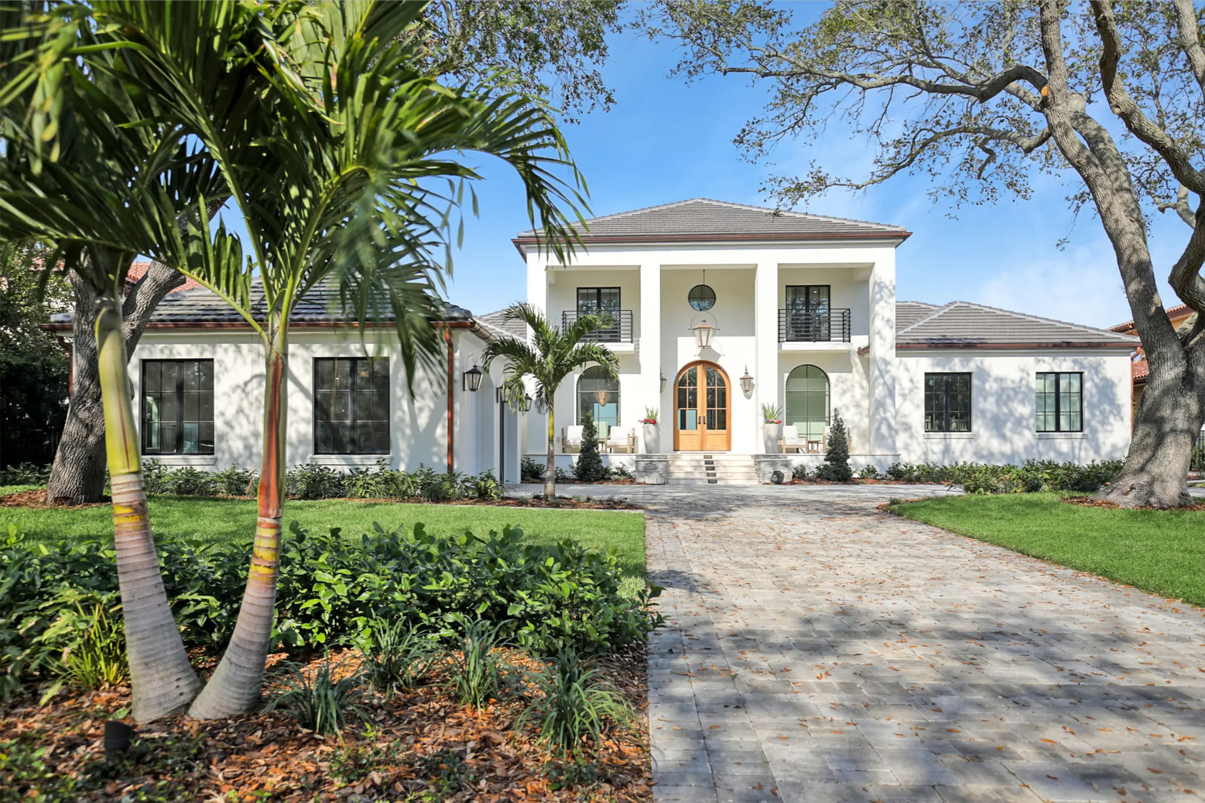 Elegant white colonial-style home with golden entry doors, palm trees, and manicured landscape in St Petersburg, FL showcasing luxury residential architecture.