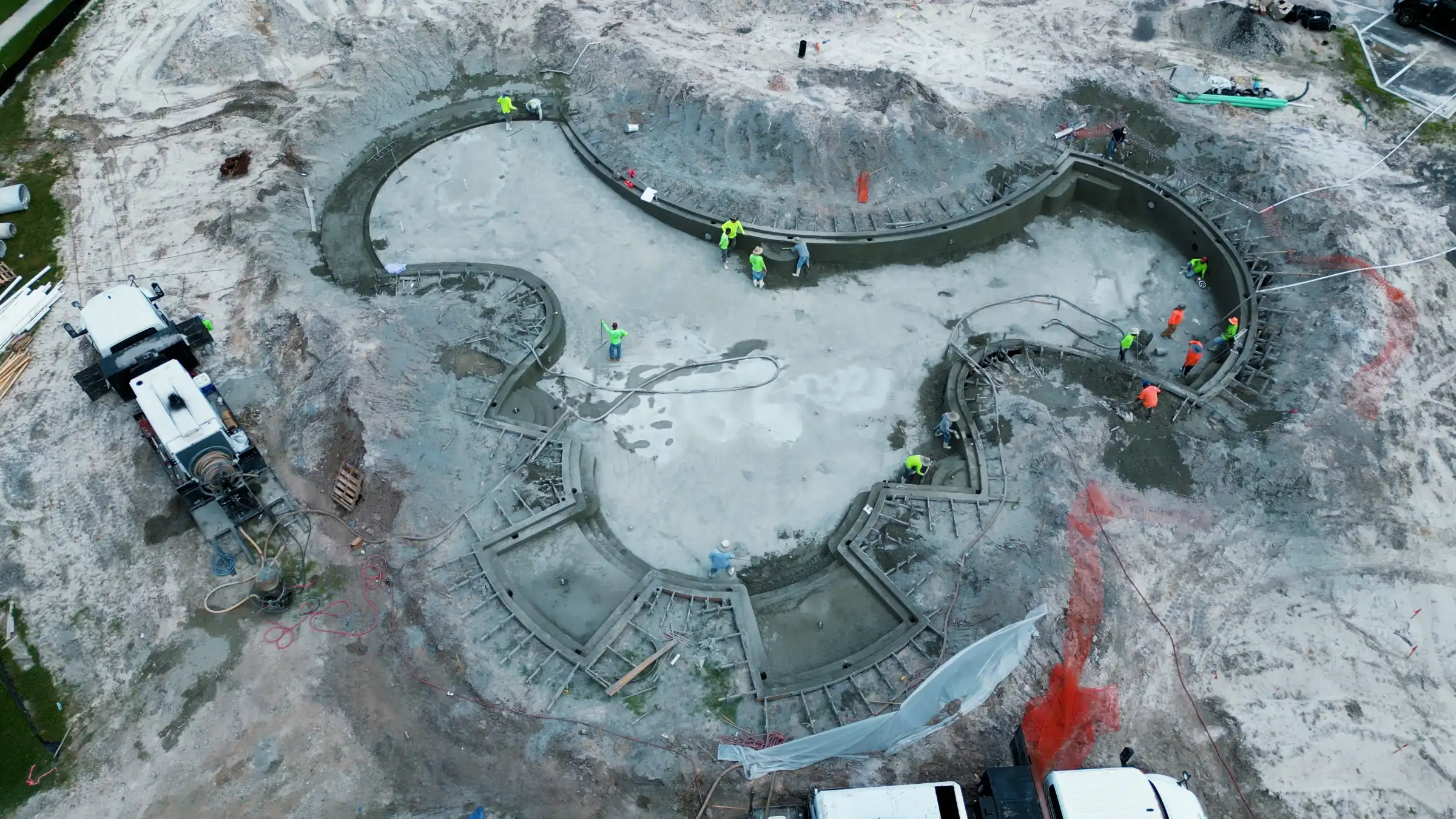 Aerial view of circular luxury pool under construction with concrete foundation, workers in safety gear, and surrounding landscape architecture site in St Petersburg.