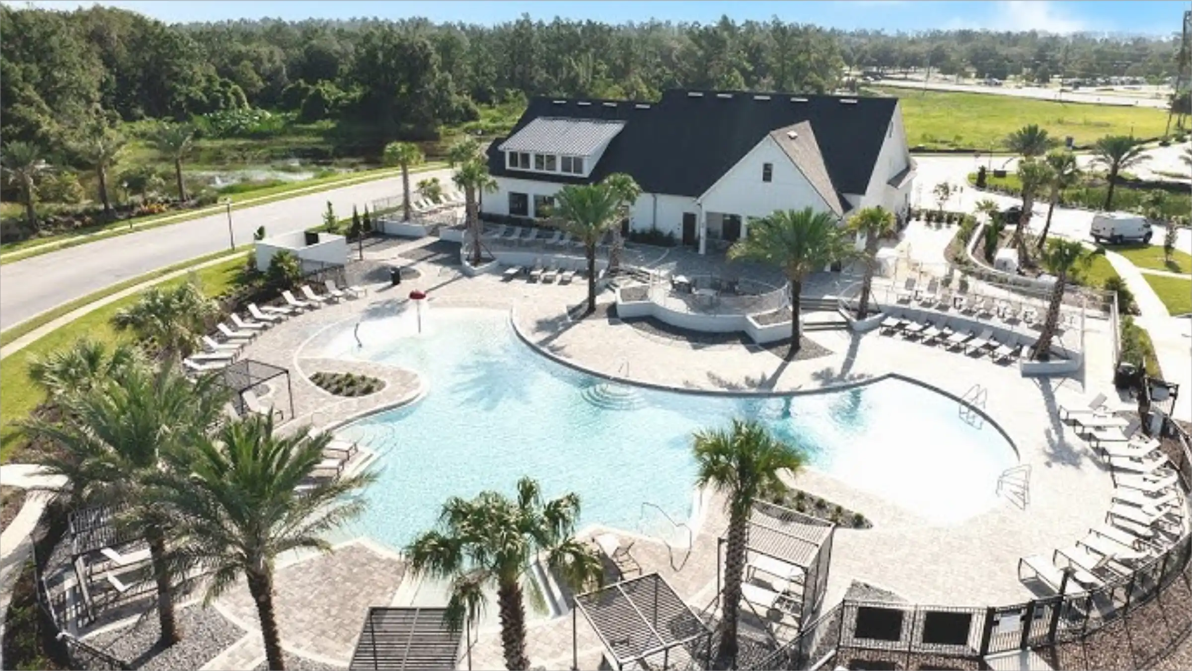 Aerial view of contemporary white home with dark roof overlooking expansive resort-style pool, sandy beaches, and palm-lined landscape in St Petersburg residential community.