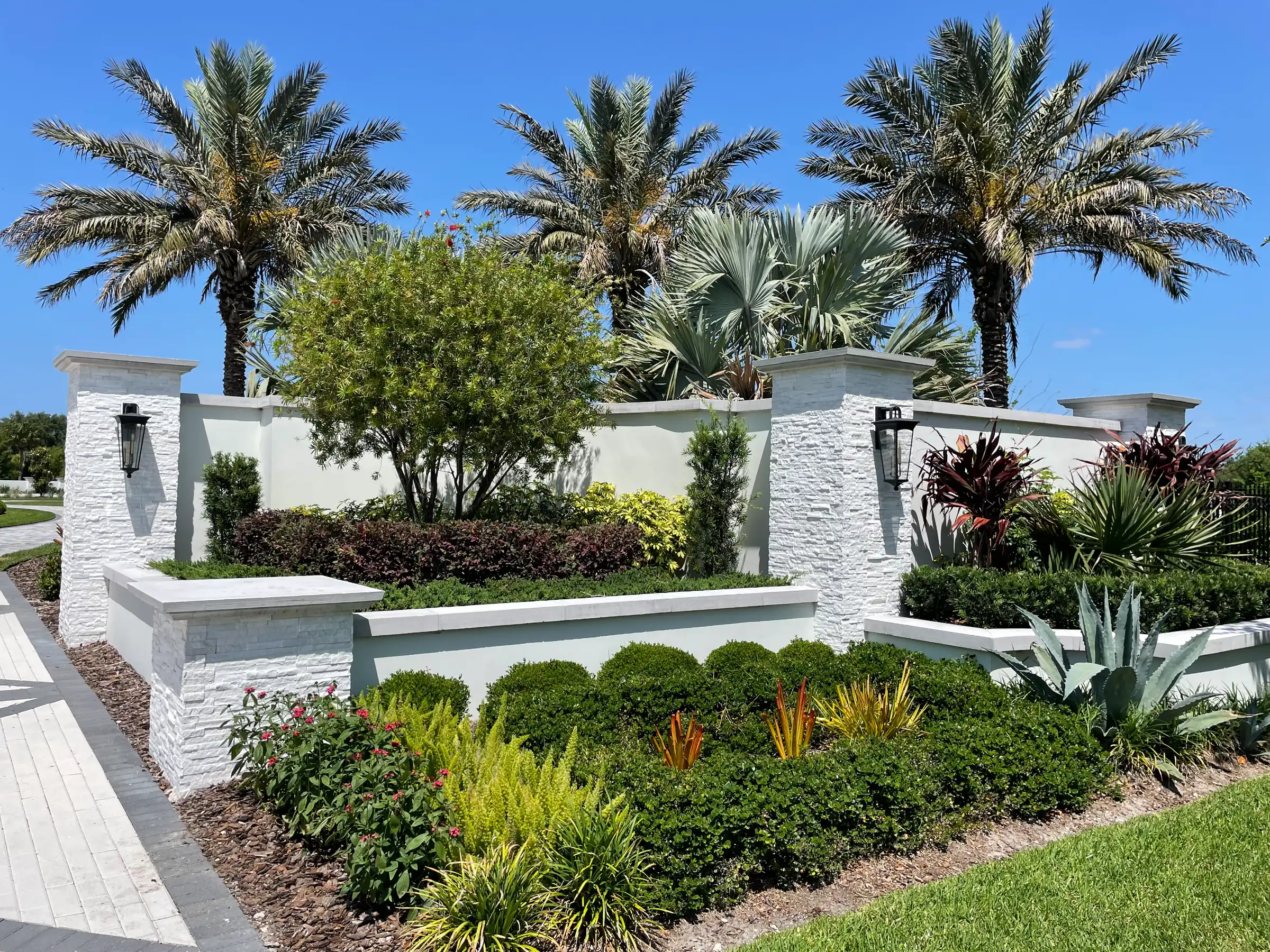 Elegant white stone residential gatehouse entrance with twin pillars, manicured hedges, and towering palm trees in St Petersburg FL luxury community.
