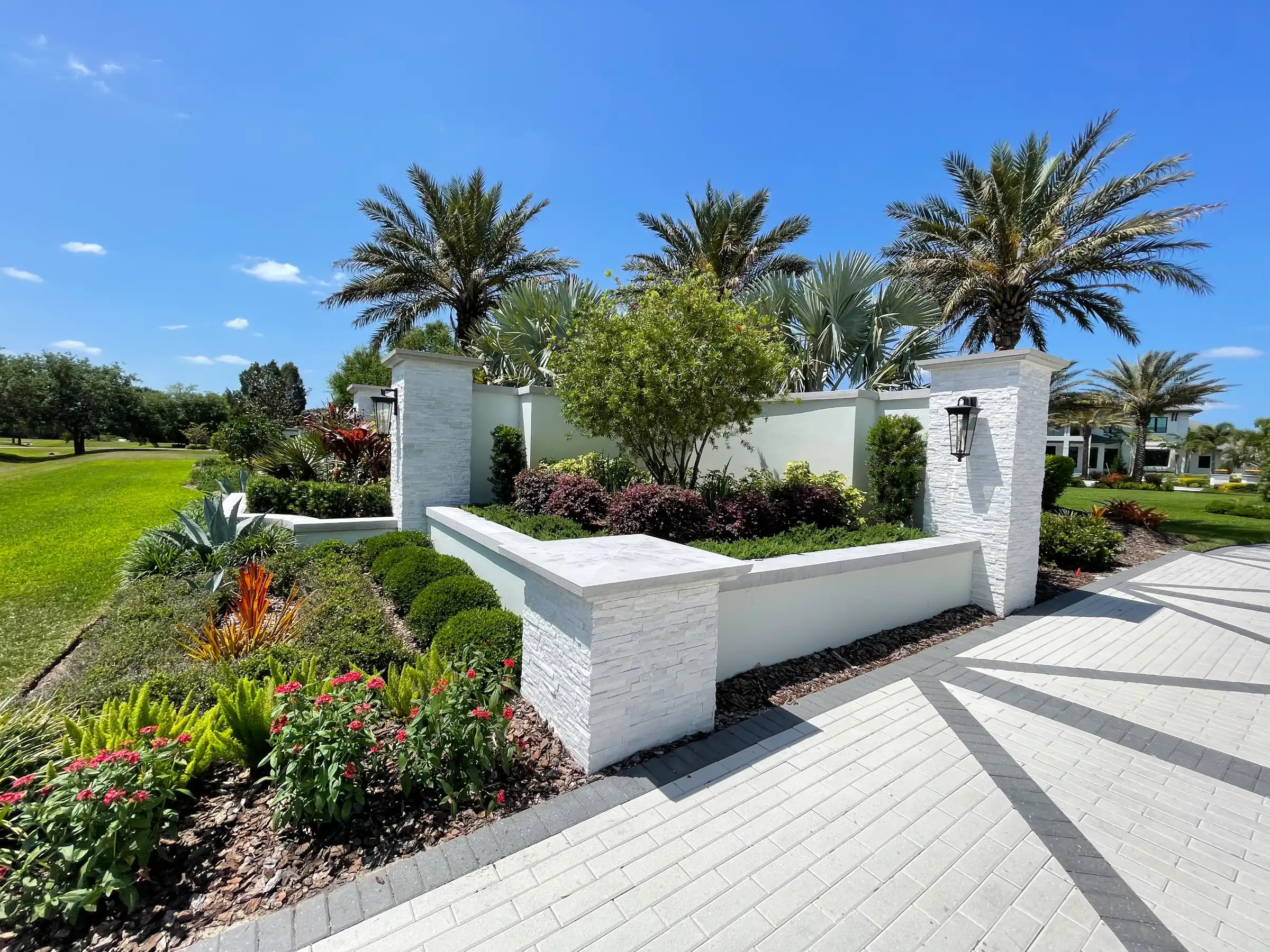 Luxury residential entry featuring white stone pillars, manicured landscape with palm trees, and patterned pavers in St Petersburg, FL