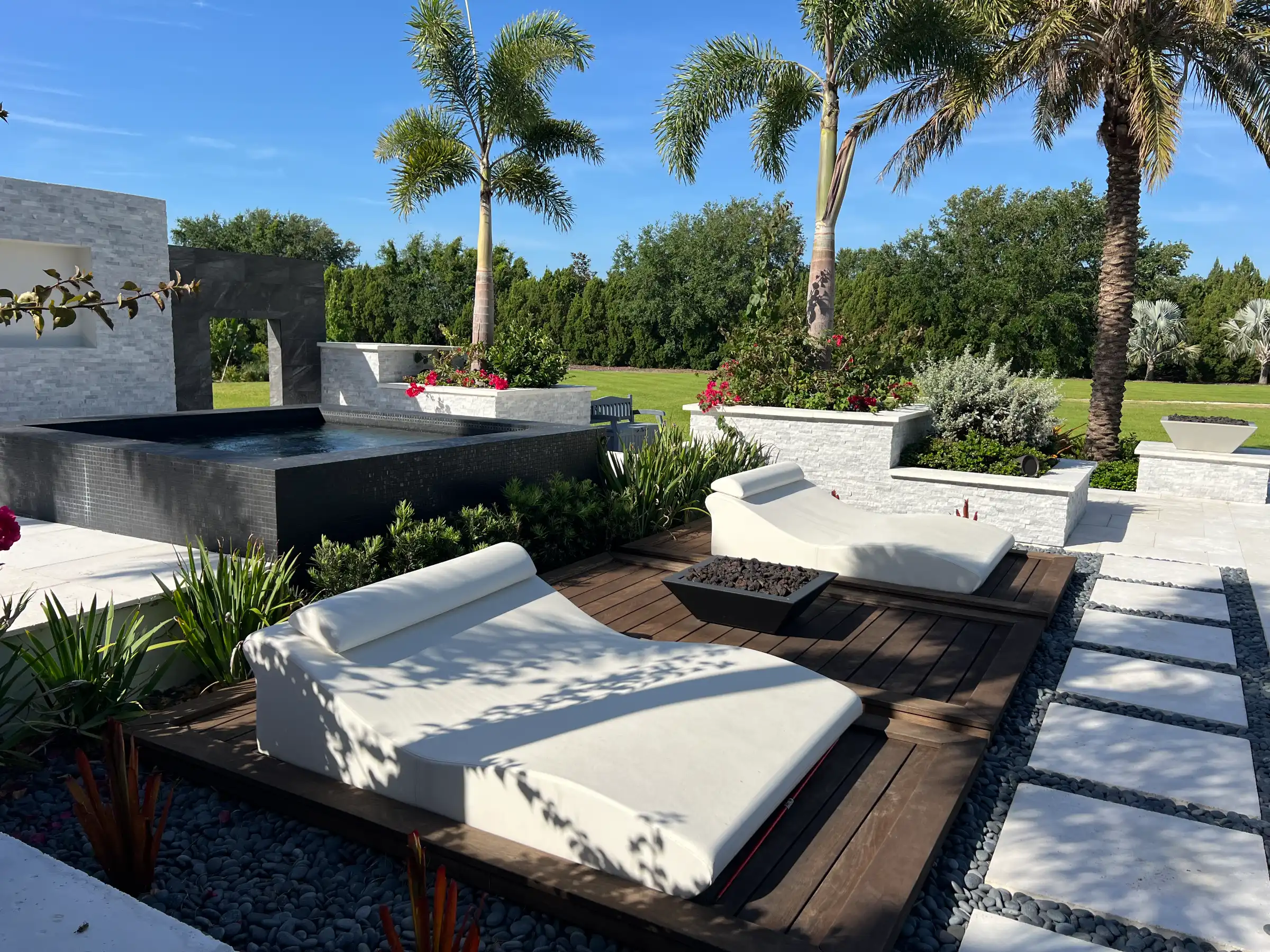 Luxury outdoor lounge area with white cushioned daybeds, dark pool, and tall palm trees overlooking manicured grounds in St Petersburg, FL.