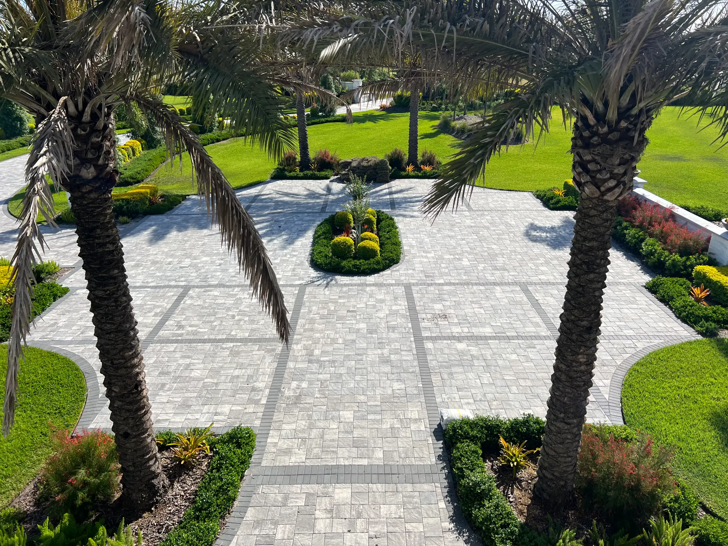 Elegant paved courtyard framed by two tall palms, featuring geometric paver patterns, manicured lawn, and professional landscape design in St Petersburg, FL.