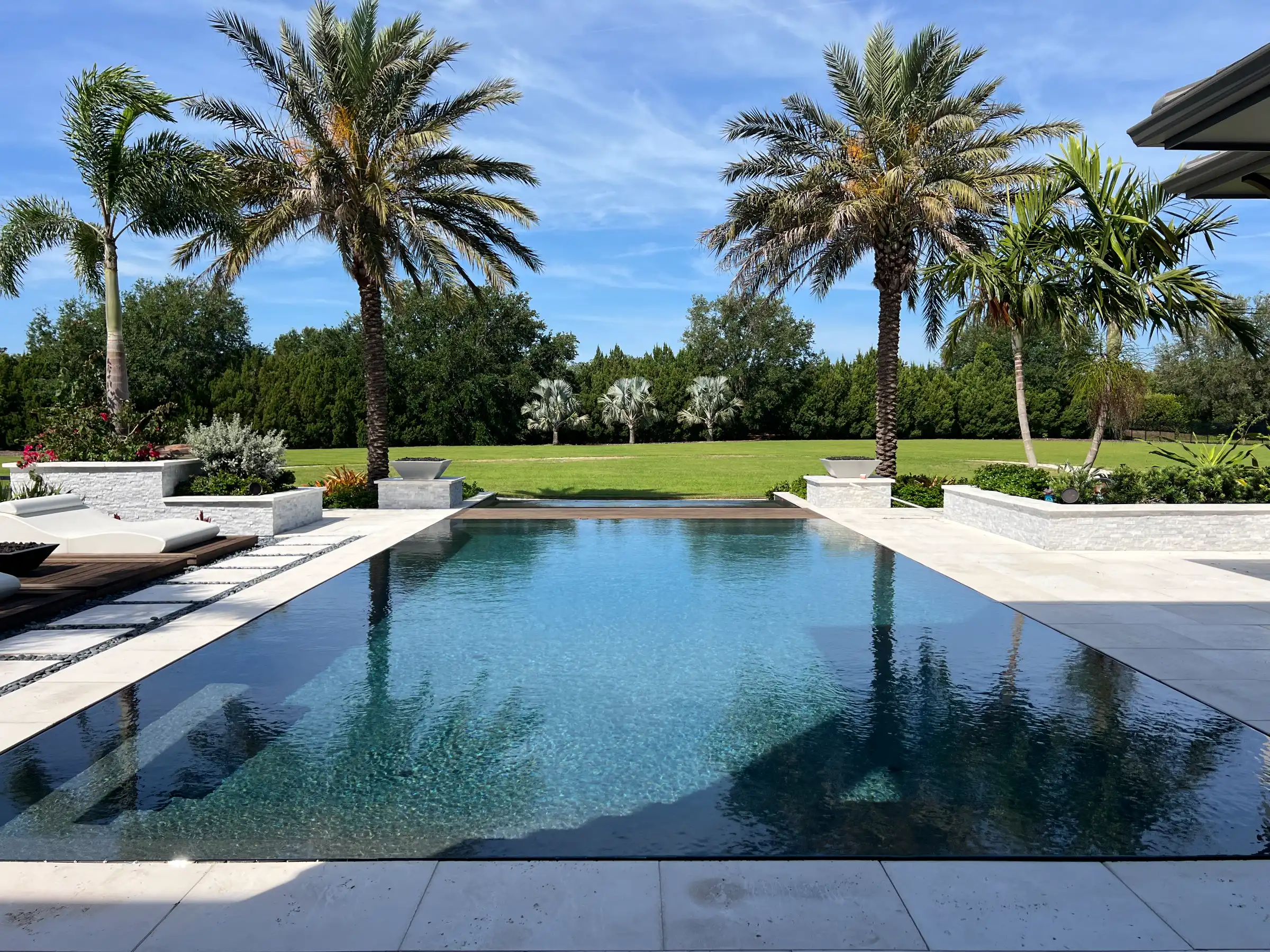 Luxury pool design with clean lines, white decking, and mature palm trees overlooking manicured lawn in St Petersburg residential community.