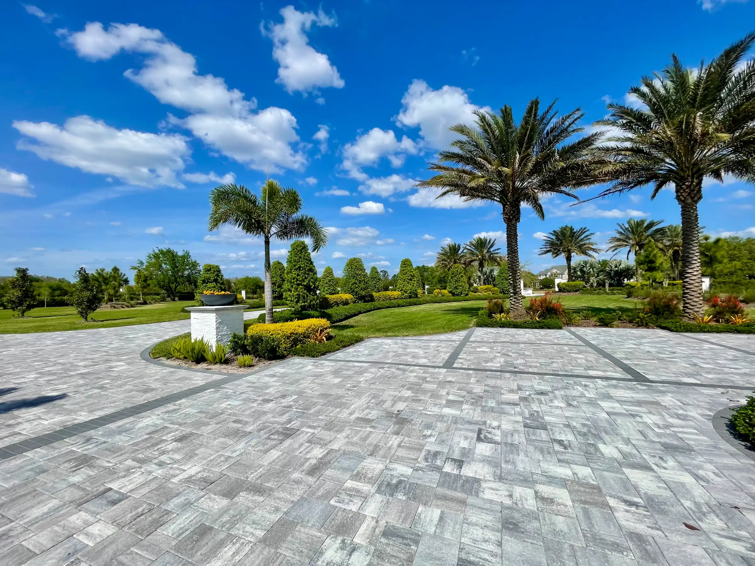 Expansive gray paver courtyard with palm trees, manicured lawn, and professional landscape design in St Petersburg residential community.