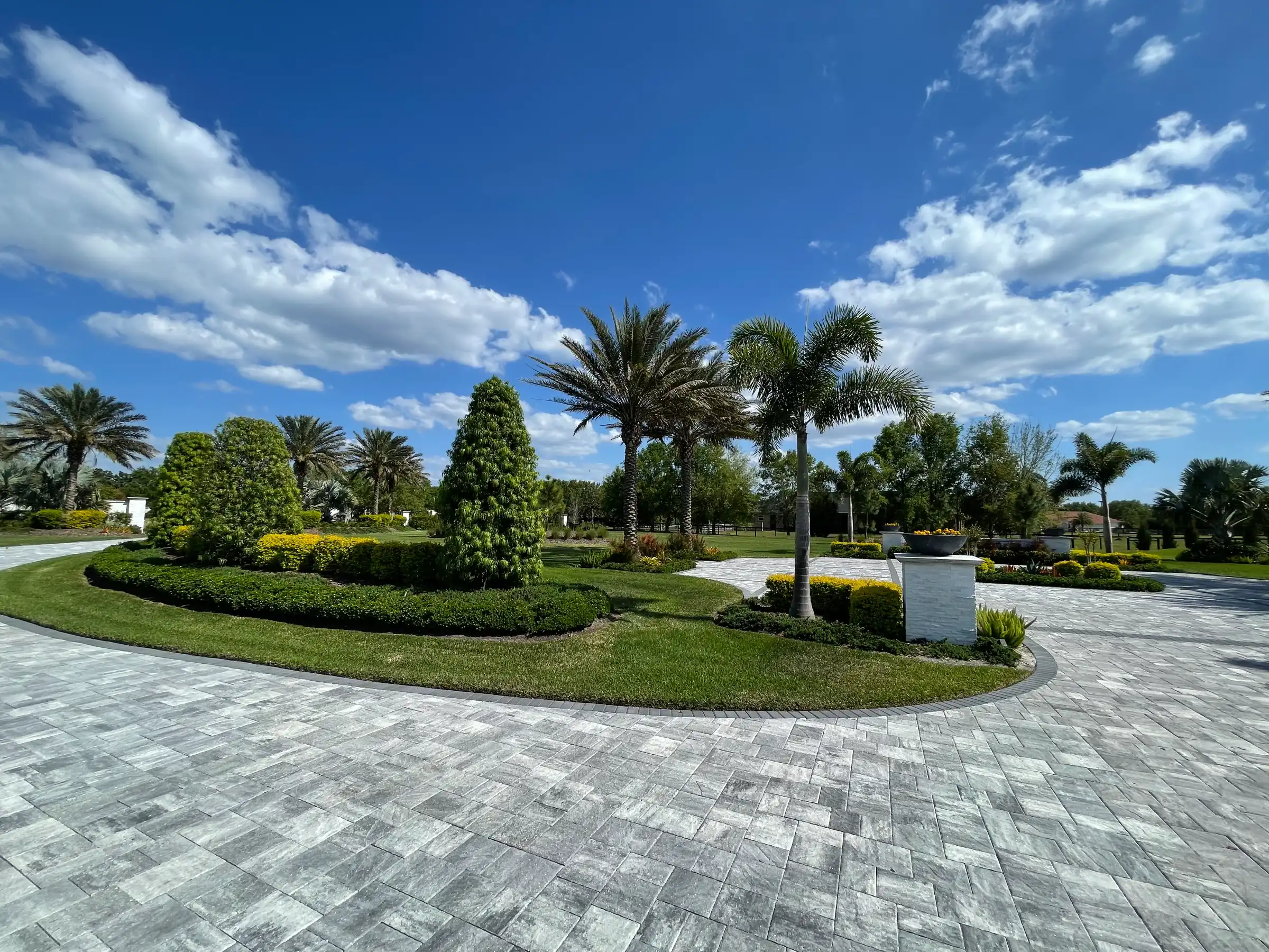 Luxury residential community in St Petersburg FL featuring expansive paver plaza with manicured lawns, palm trees, and sophisticated landscape architecture design.