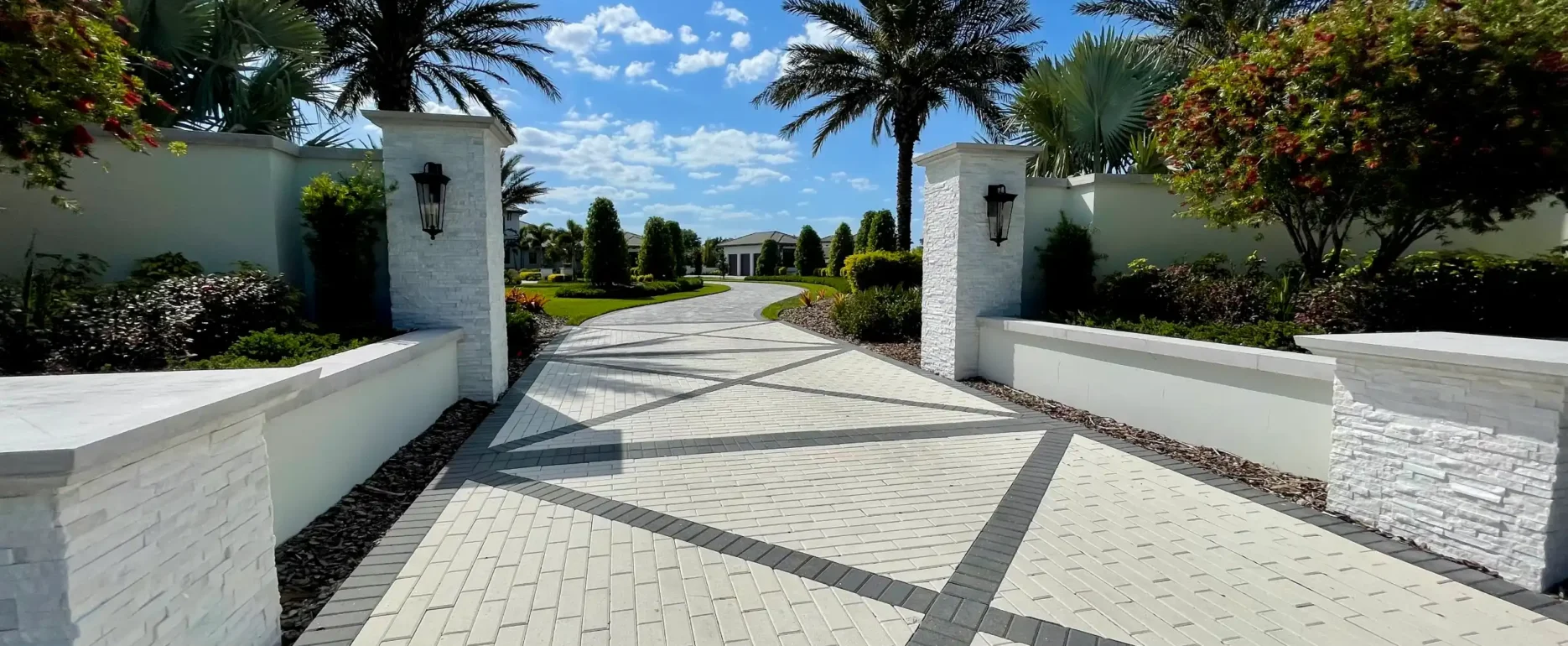 Elegant paved driveway with white brick entry gates and palm trees leading to luxury residential community in St Petersburg, FL