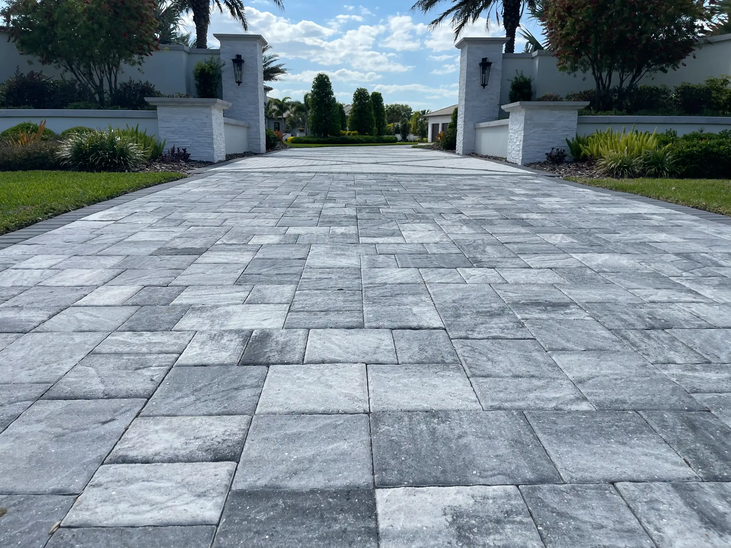 Elegant gray paver driveway with symmetrical white stone pillars and manicured landscaping in St Petersburg FL luxury residential community