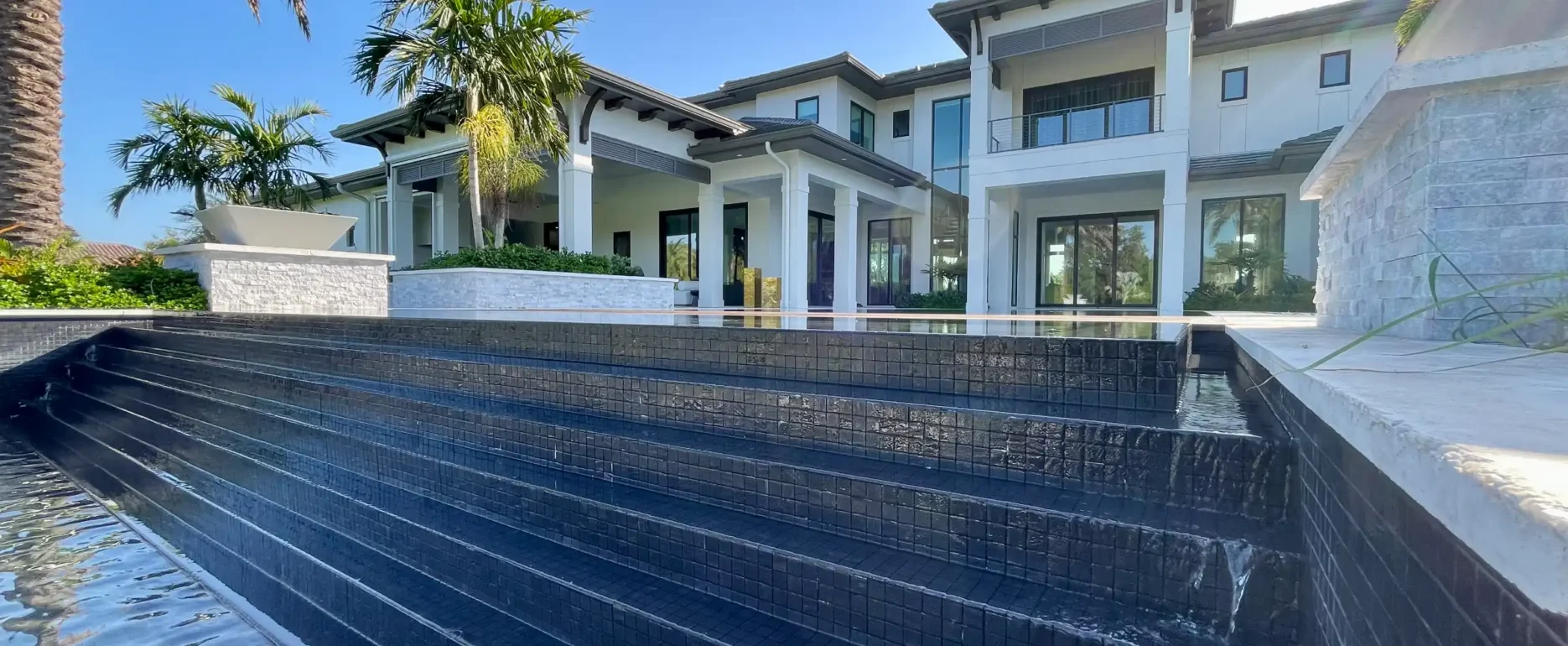 Modern luxury home with white architecture and dark-tiled infinity pool overlooking lush landscape in St Petersburg residential community