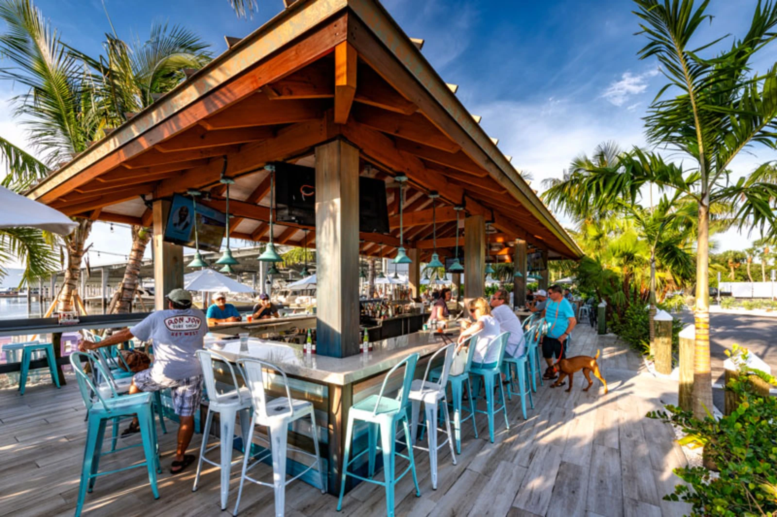 Luxury waterfront restaurant pavilion with wooden beams, turquoise and white metal chairs, and palm trees in St. Petersburg, FL.