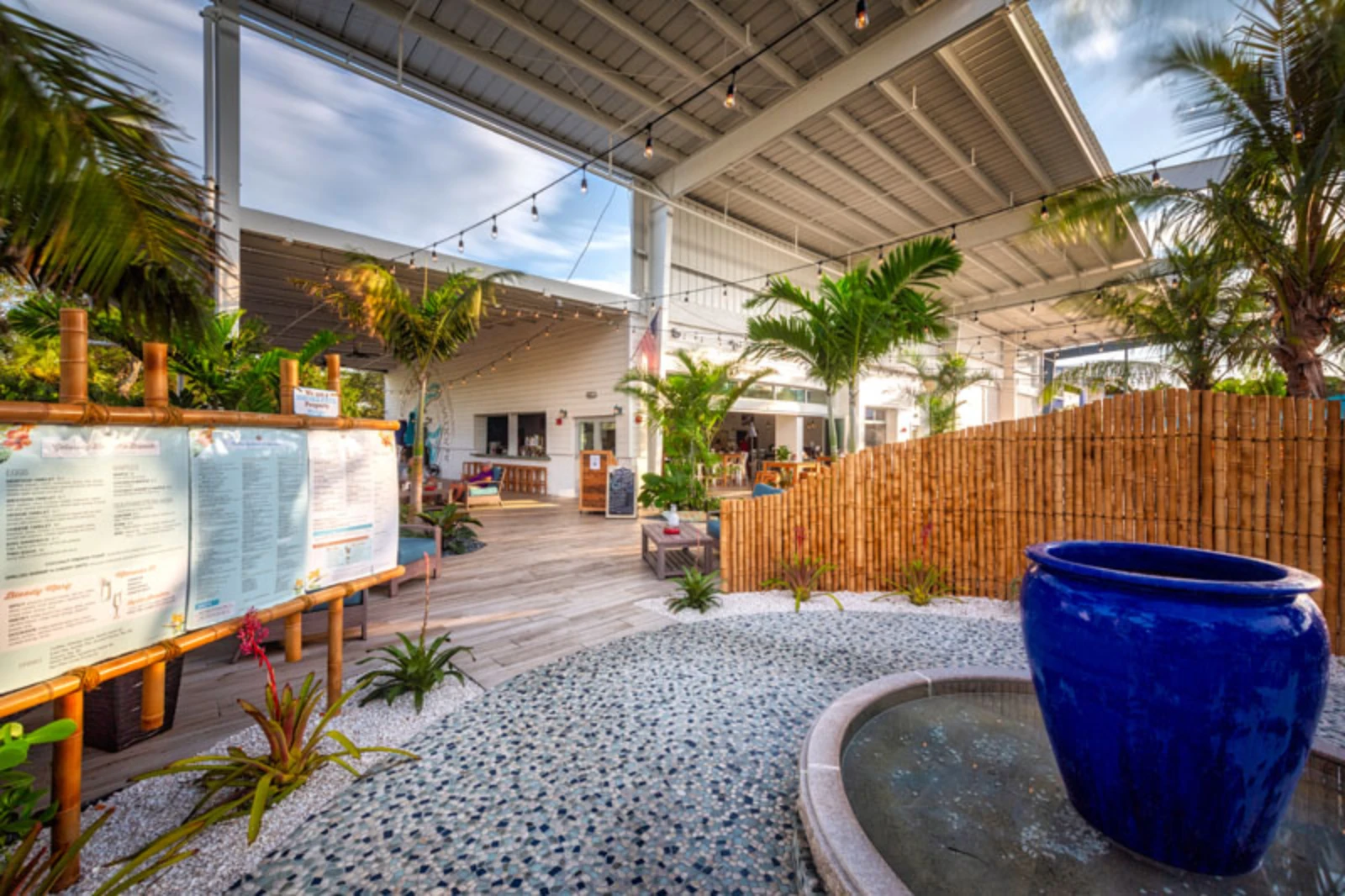 Covered outdoor patio featuring blue ceramic vessels, tropical plants, and wooden deck in luxury residential landscape design.