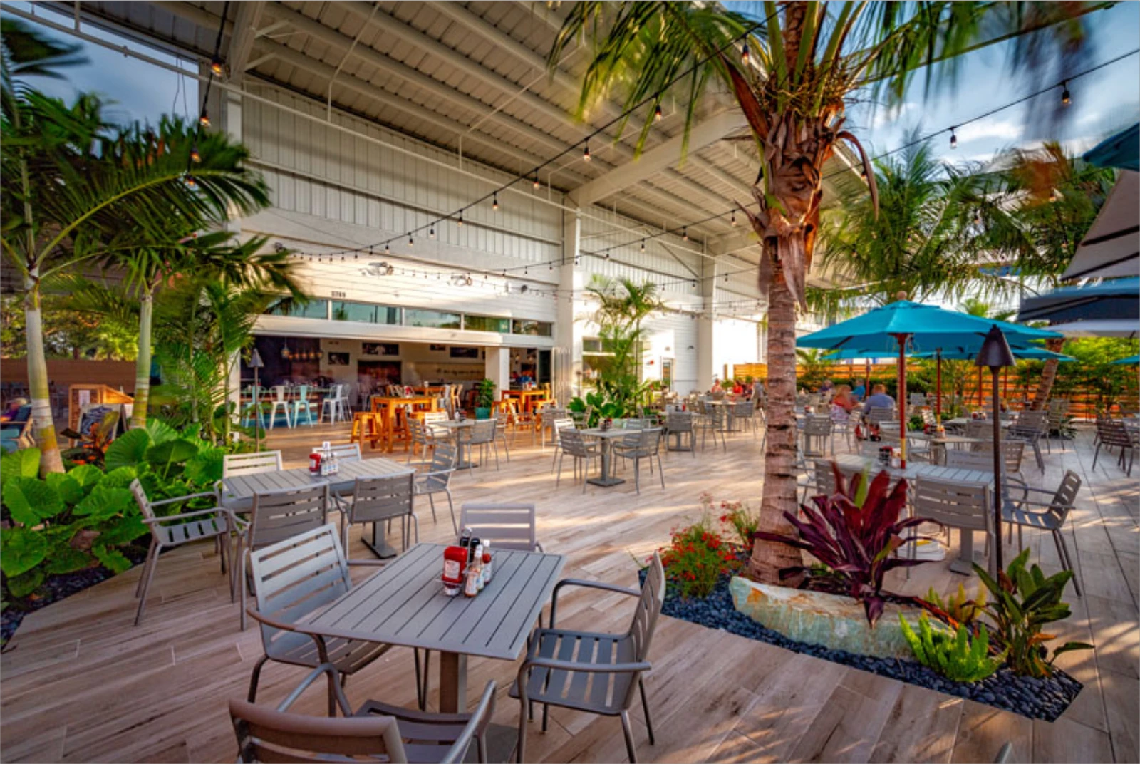 Luxury outdoor dining area under metal pavilion with palm trees, gray furniture, and blue umbrellas in St Petersburg, FL.