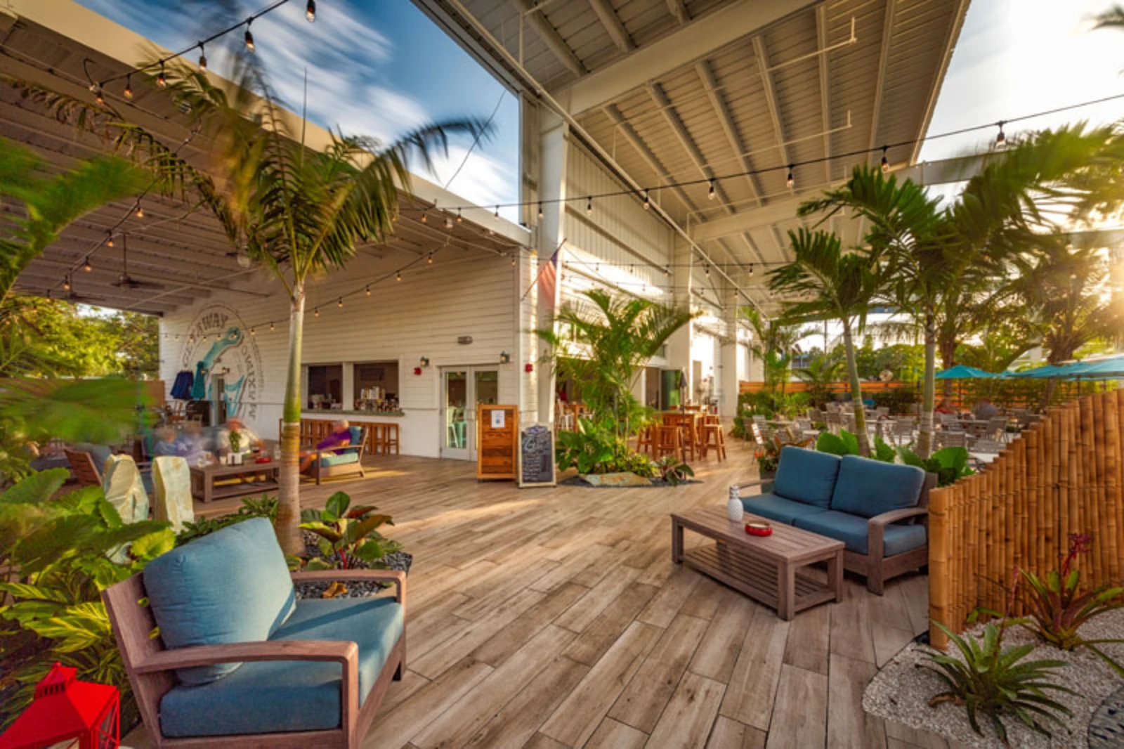 Luxury covered patio with wooden deck, blue cushioned seating, tropical plants, and modern shade structure in St Petersburg FL residential community.