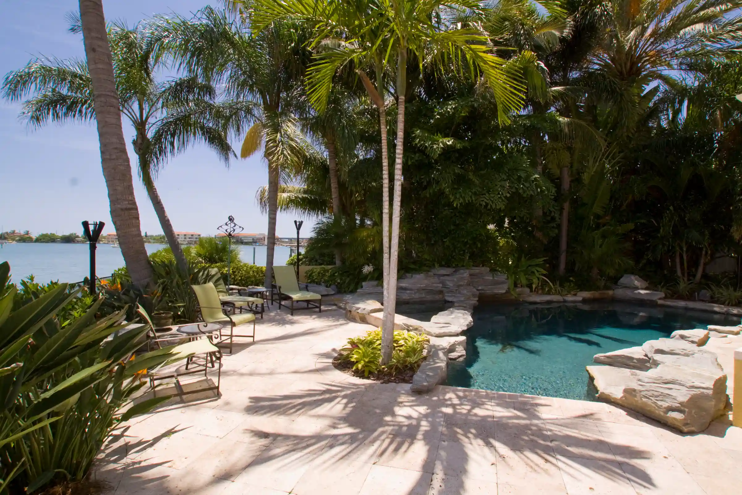 Luxury poolside patio with turquoise pool, palm trees, lounge seating, and waterfront views in St Petersburg residential community.