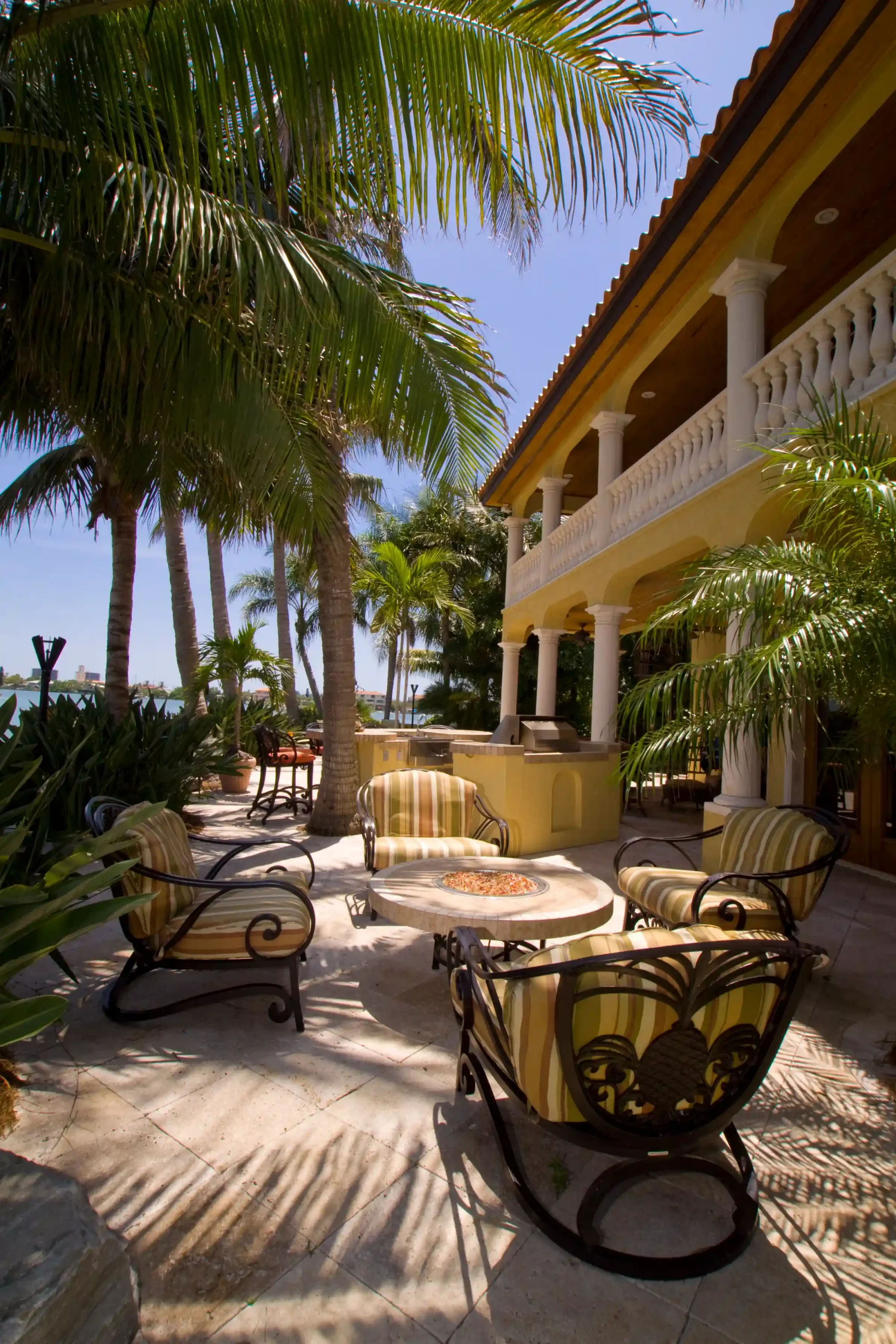 Luxury coastal terrace with striped lounge chairs, fire pit table, and palm trees overlooking waterfront in St Petersburg FL