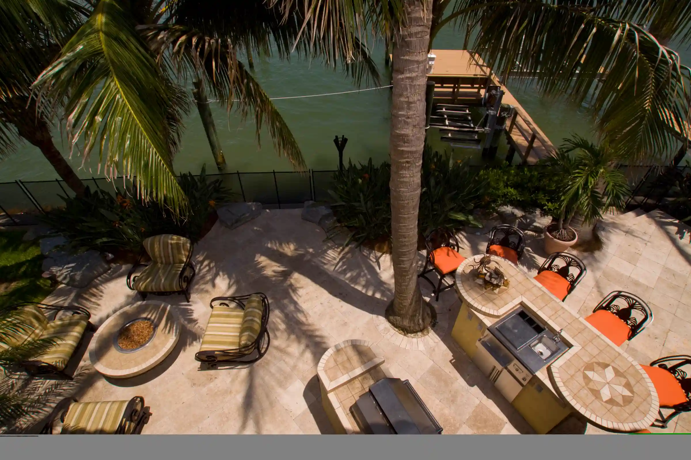 Aerial view of luxury waterfront patio with orange lounge chairs, palm trees, and tiled pool deck overlooking turquoise water in St Petersburg residential community.