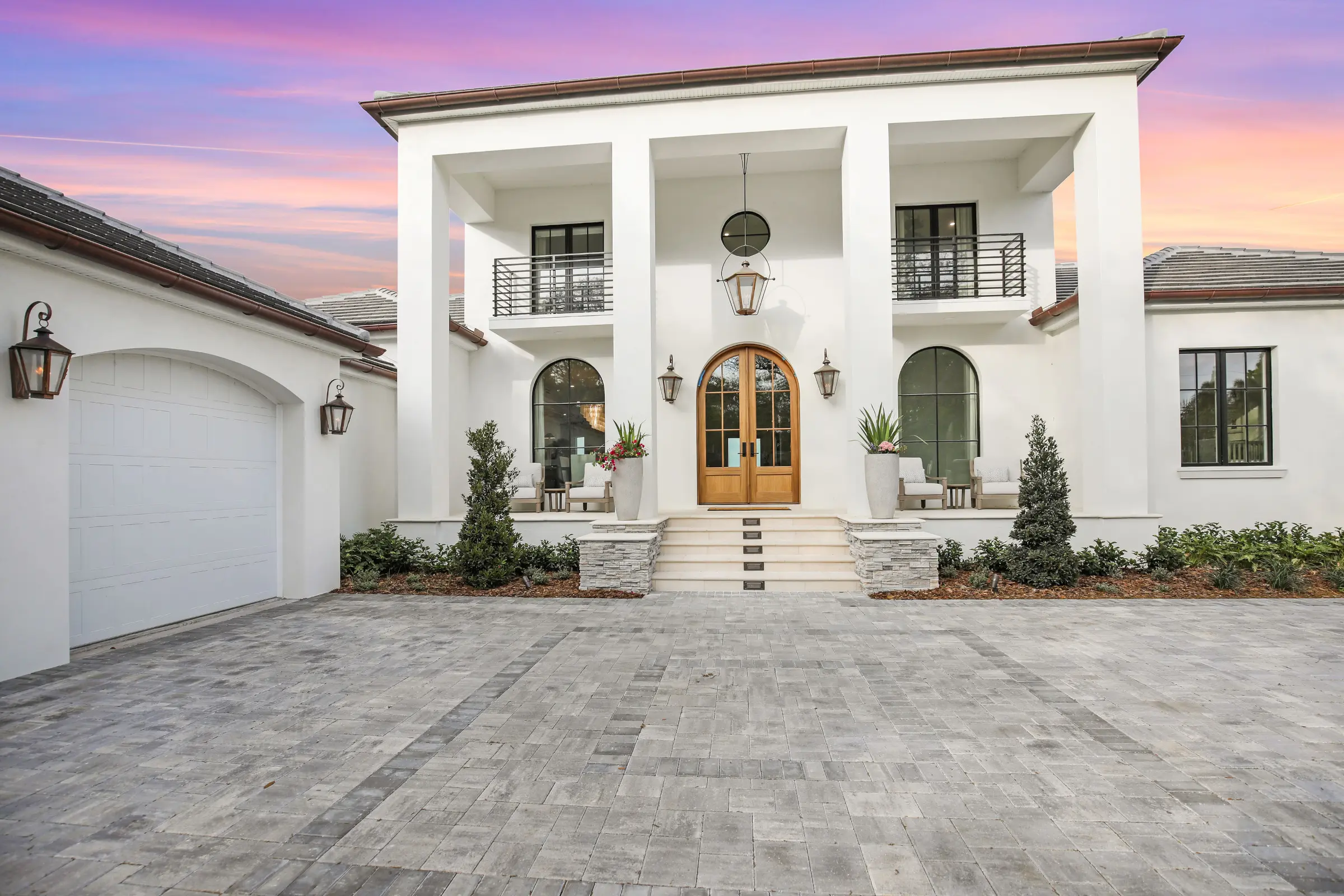 Contemporary white stucco residential home with arched wooden doors, multiple balconies, and elegant paver driveway in St Petersburg, Florida luxury community.