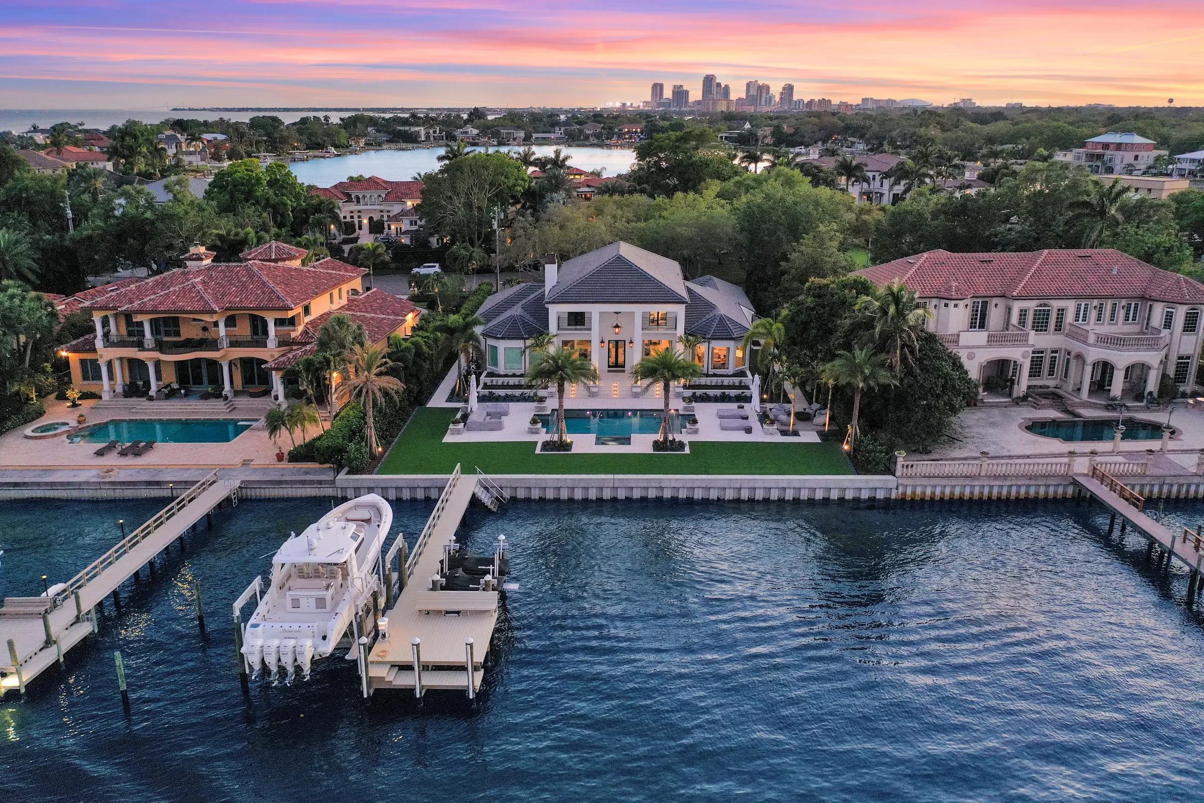 Luxury waterfront home with modern architecture, pool, and private dock on St Petersburg FL waterway at dusk with city skyline beyond