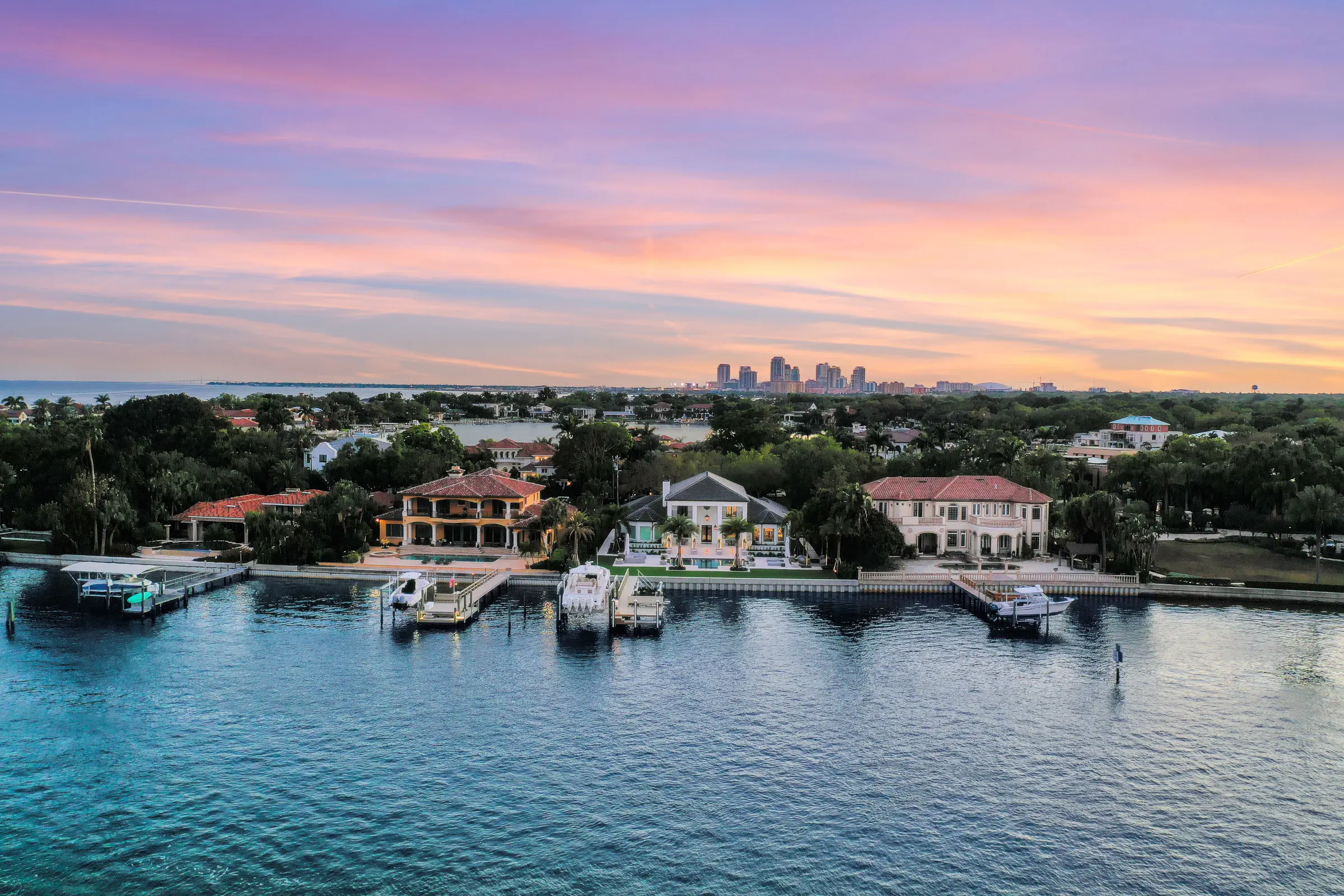 Luxury waterfront homes with private docks at sunset overlooking St Petersburg skyline, showcasing premium residential landscape architecture and pool design.