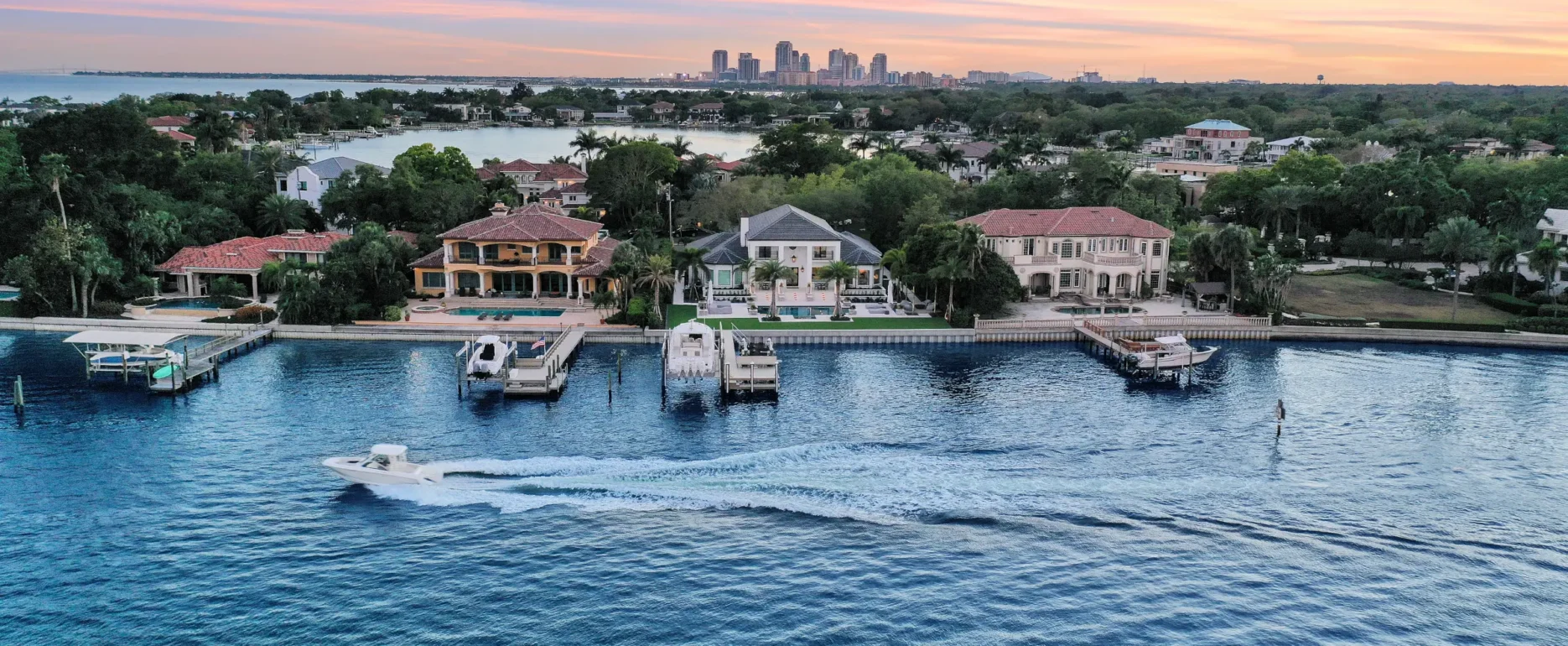 Luxury waterfront homes with private docks overlooking bay toward St Petersburg skyline at sunset, featuring pool design and landscape architecture.
