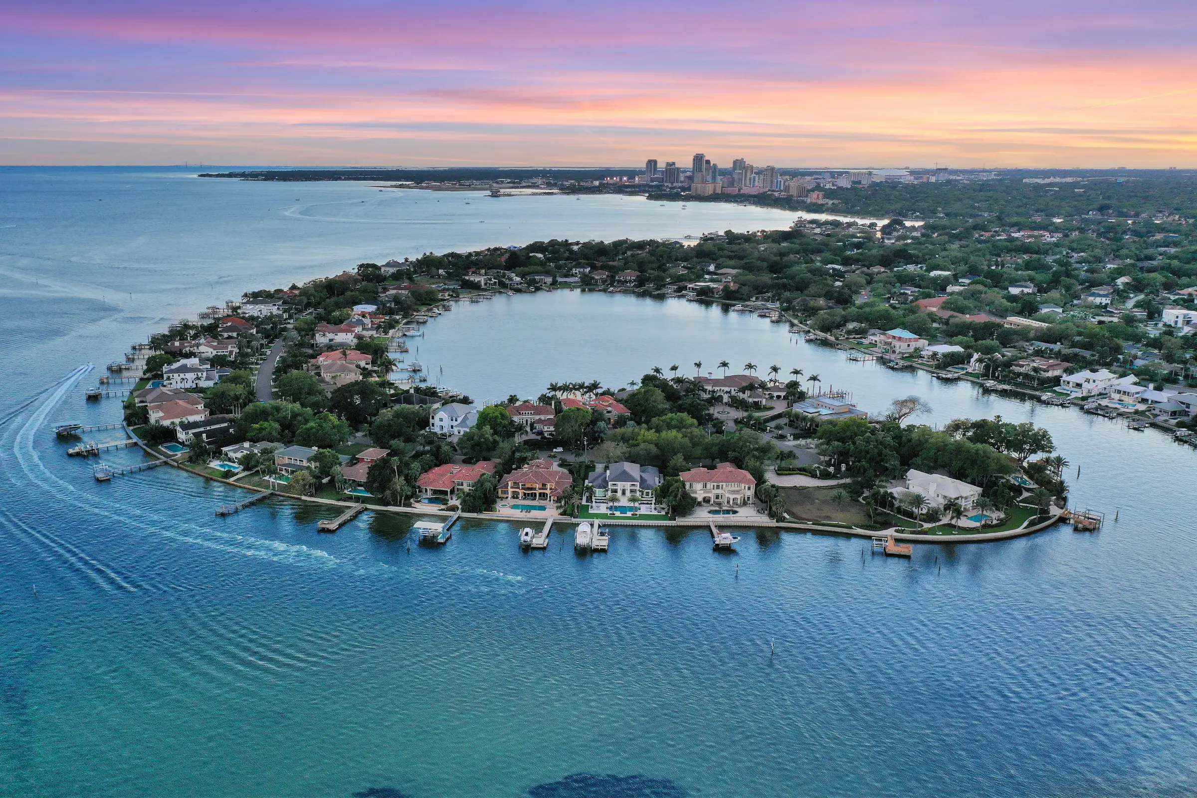 Aerial view of luxury waterfront residential community in St Petersburg, FL with bay homes, private docks, and downtown skyline at dusk.
