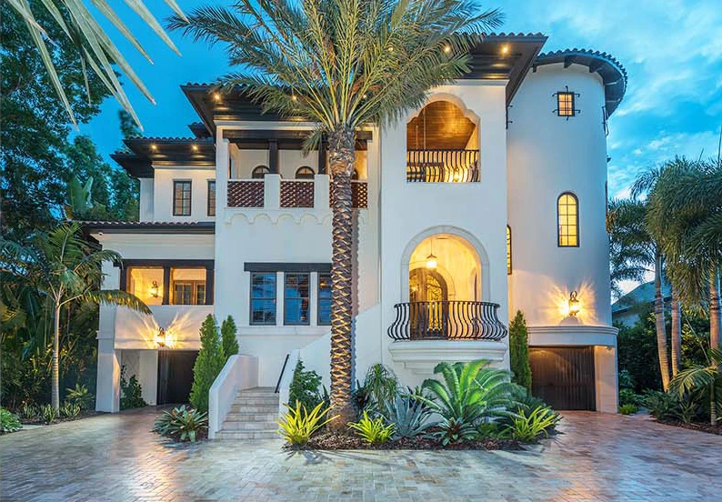Elegant white Spanish Colonial residence with curved tower, palm trees, and illuminated arched entryways in St Petersburg luxury residential community.
